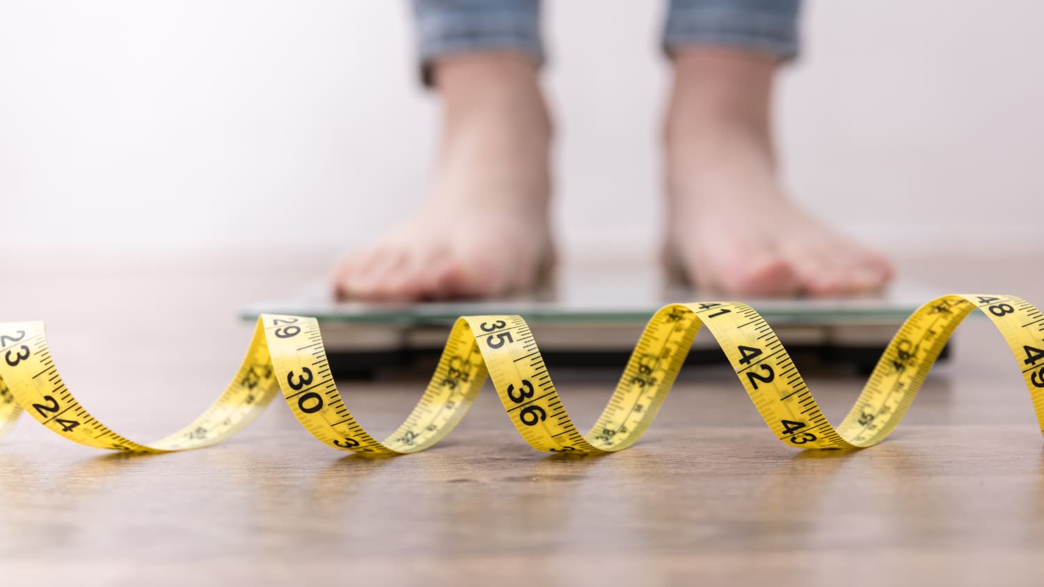 Person standing on a scale with tape measure unfurled on floor.