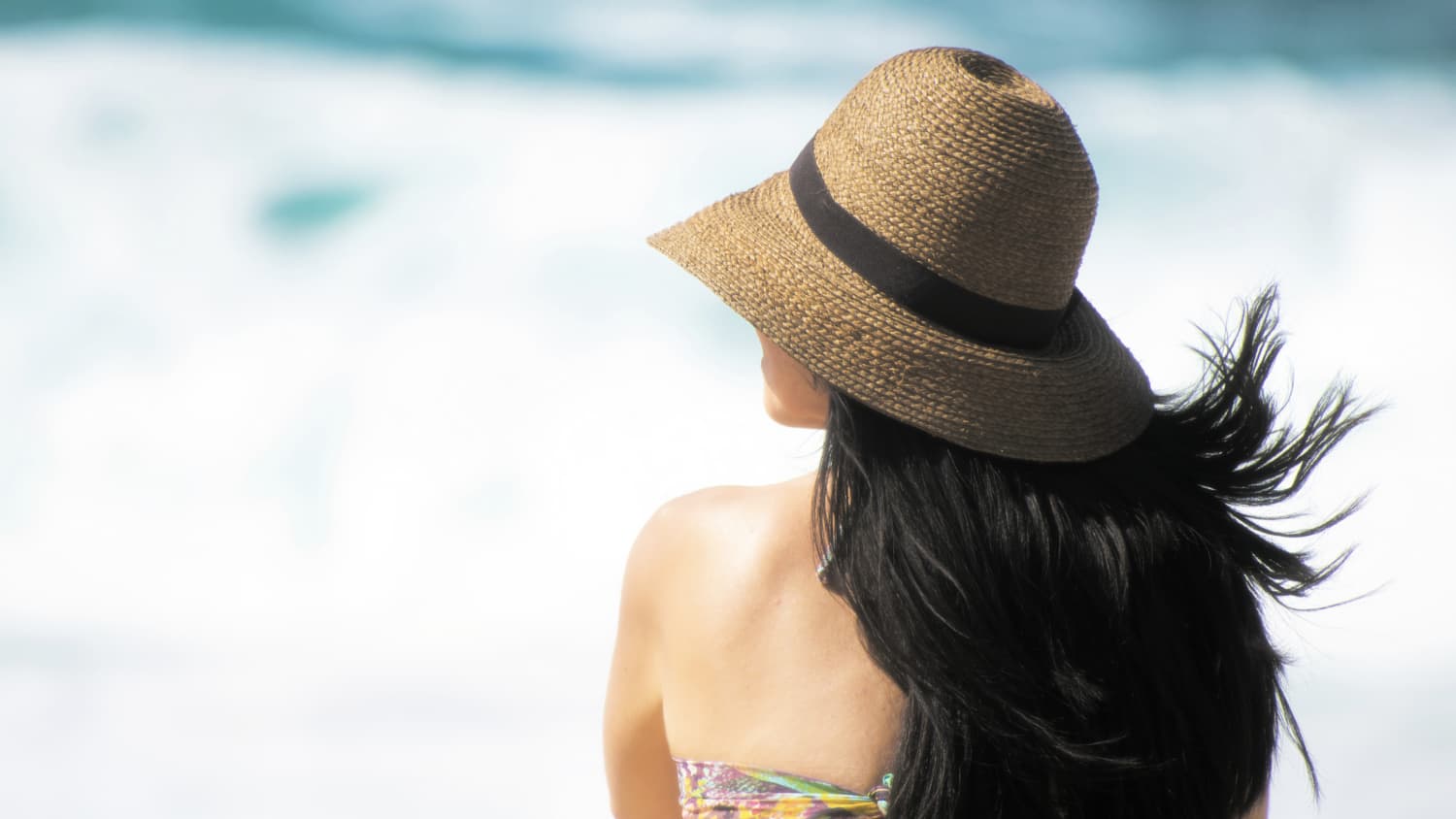 Woman on beach with long dark hair wearing hat.