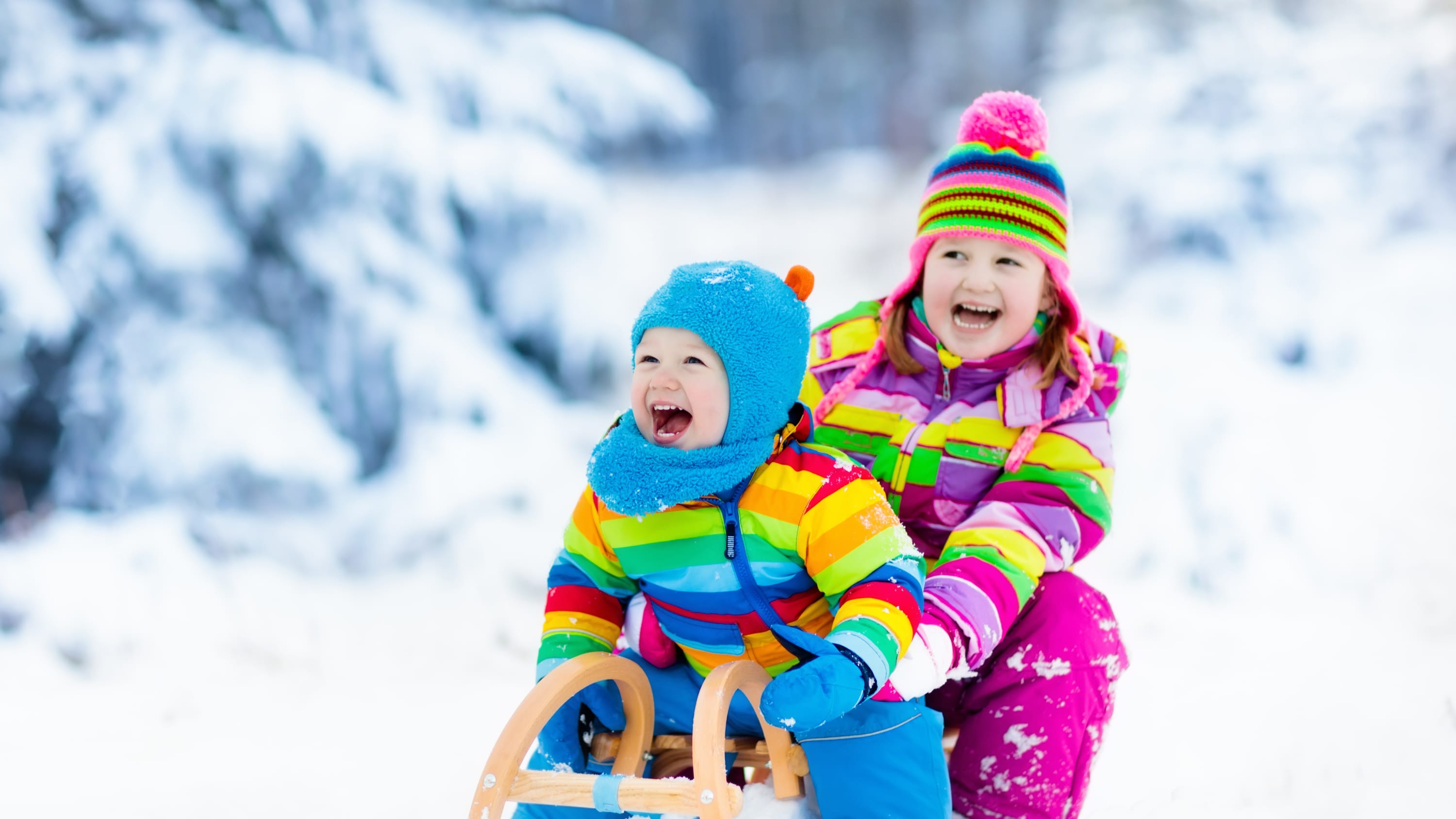 Two children are sledding while wearing colorful outerwear.