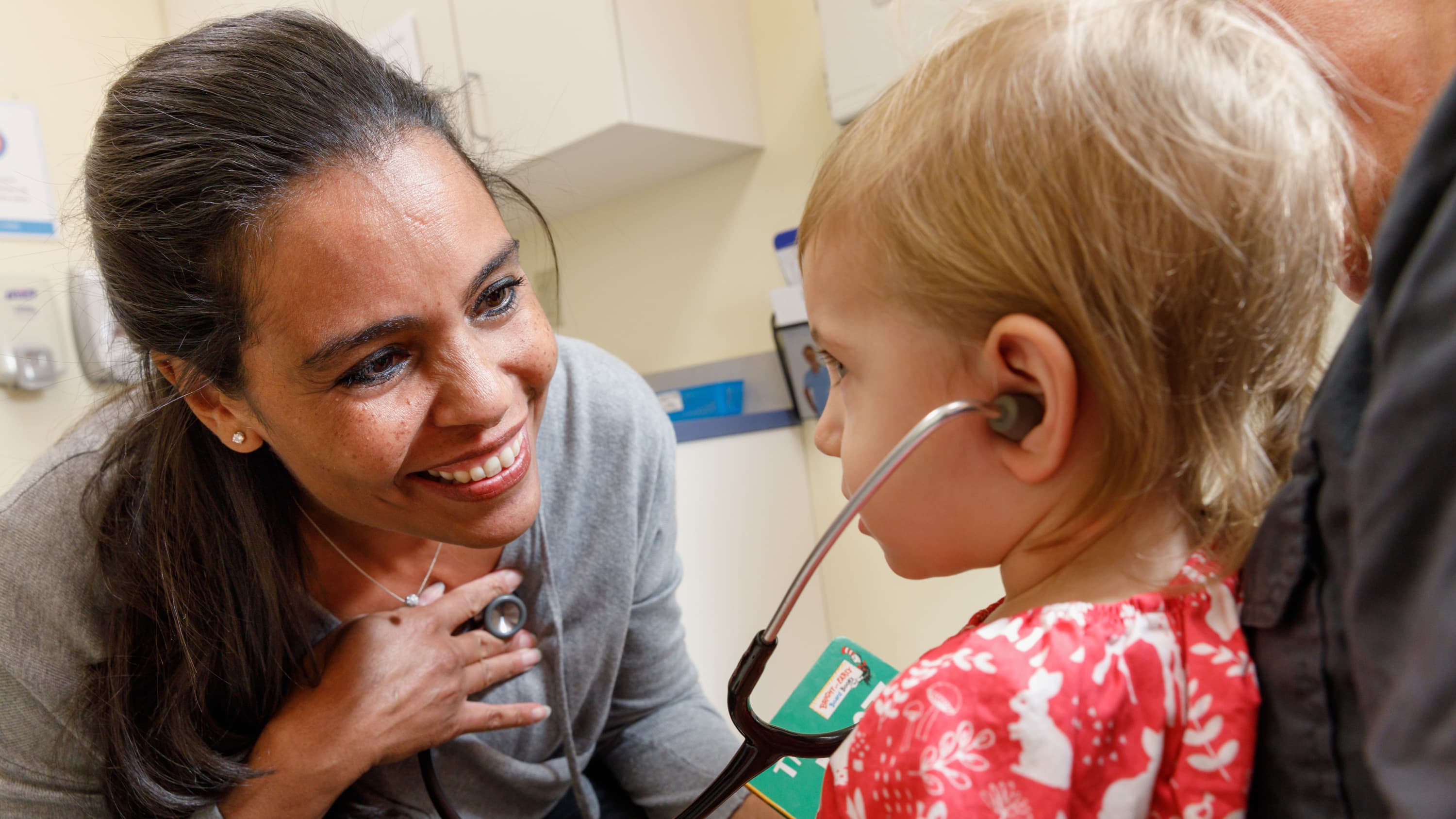 Dr. Annette Cameron is making a young patient feel comfortable by having her listen to her heartbeat using a stethoscope.