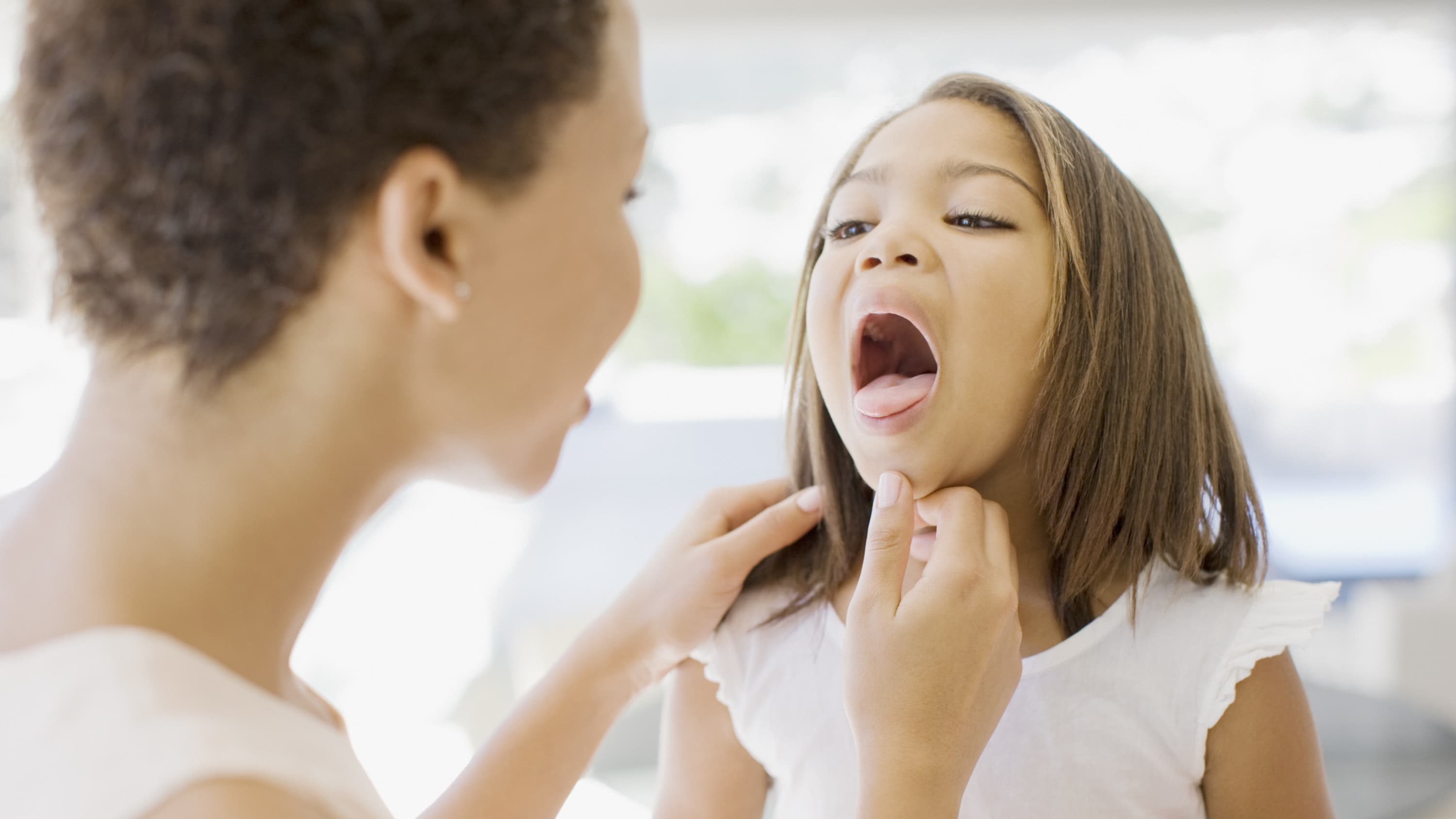 A mother checks her daughter's sore throat before consulting the doctor about a tonsillectomy.