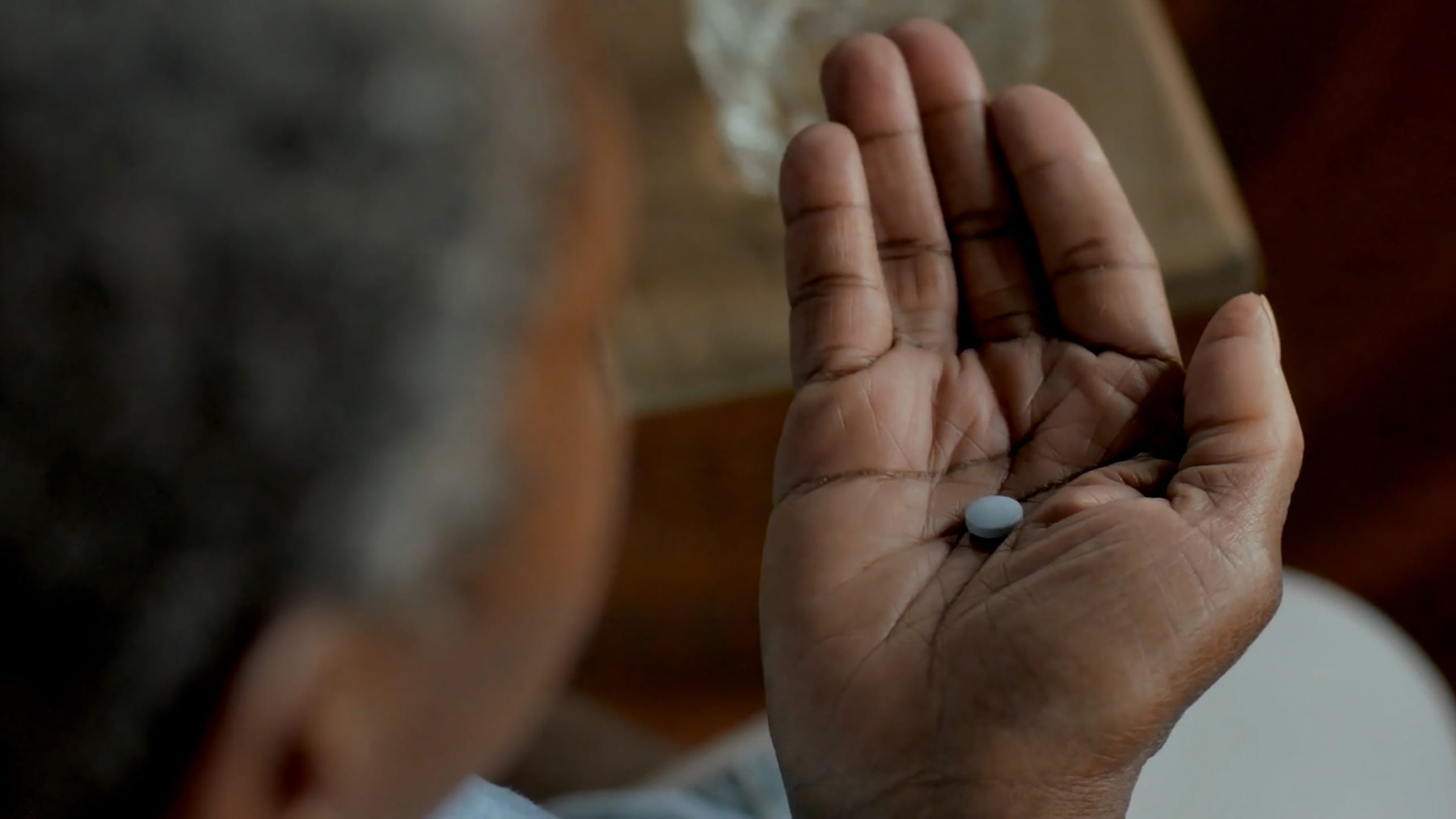 African American woman with greying hair looking down at a light blue pill in the palm of her hand