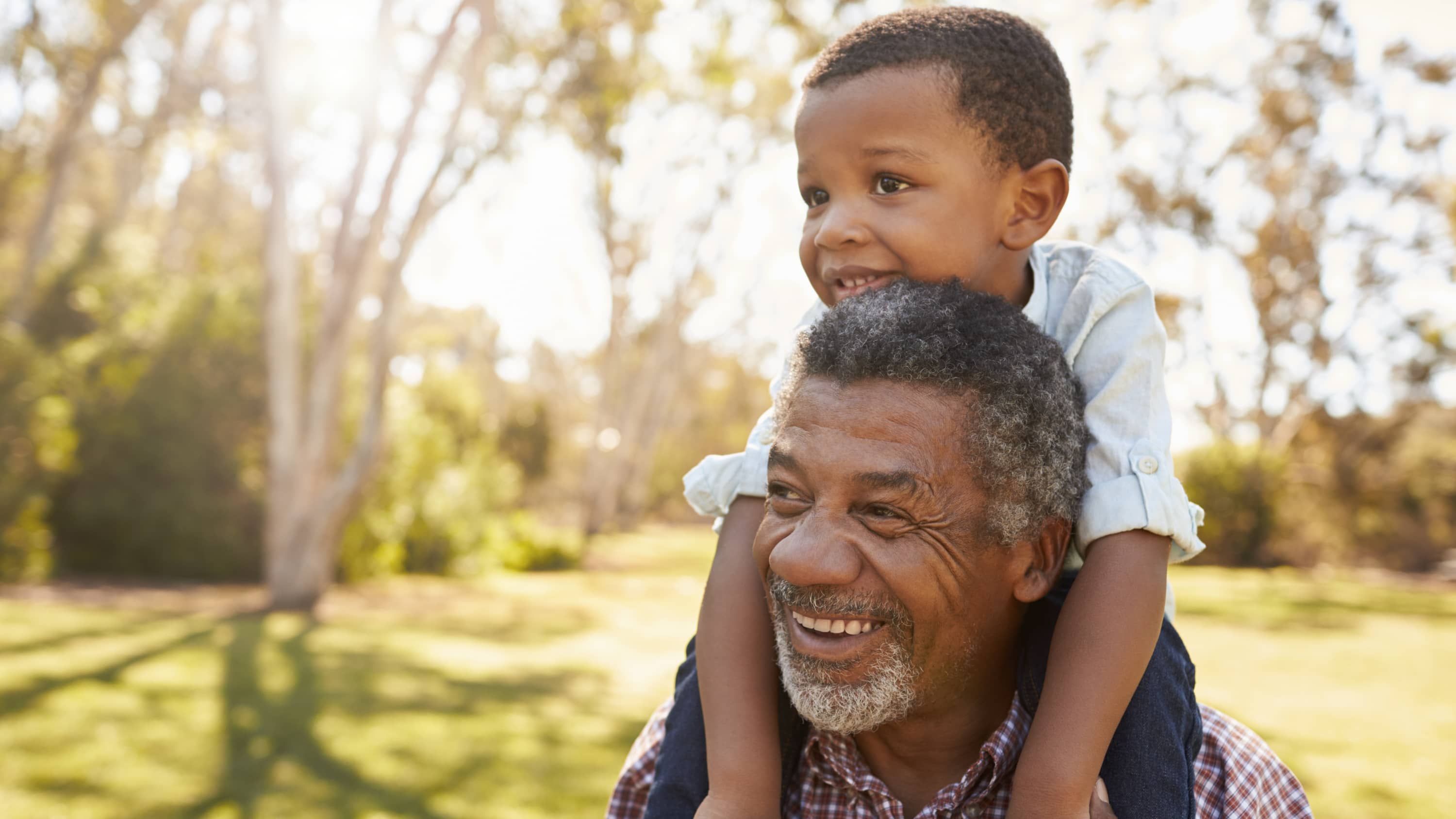 older man smiling with grandson on his shoulder after treatment for Chronic Myeloid Leukemia (CML)
