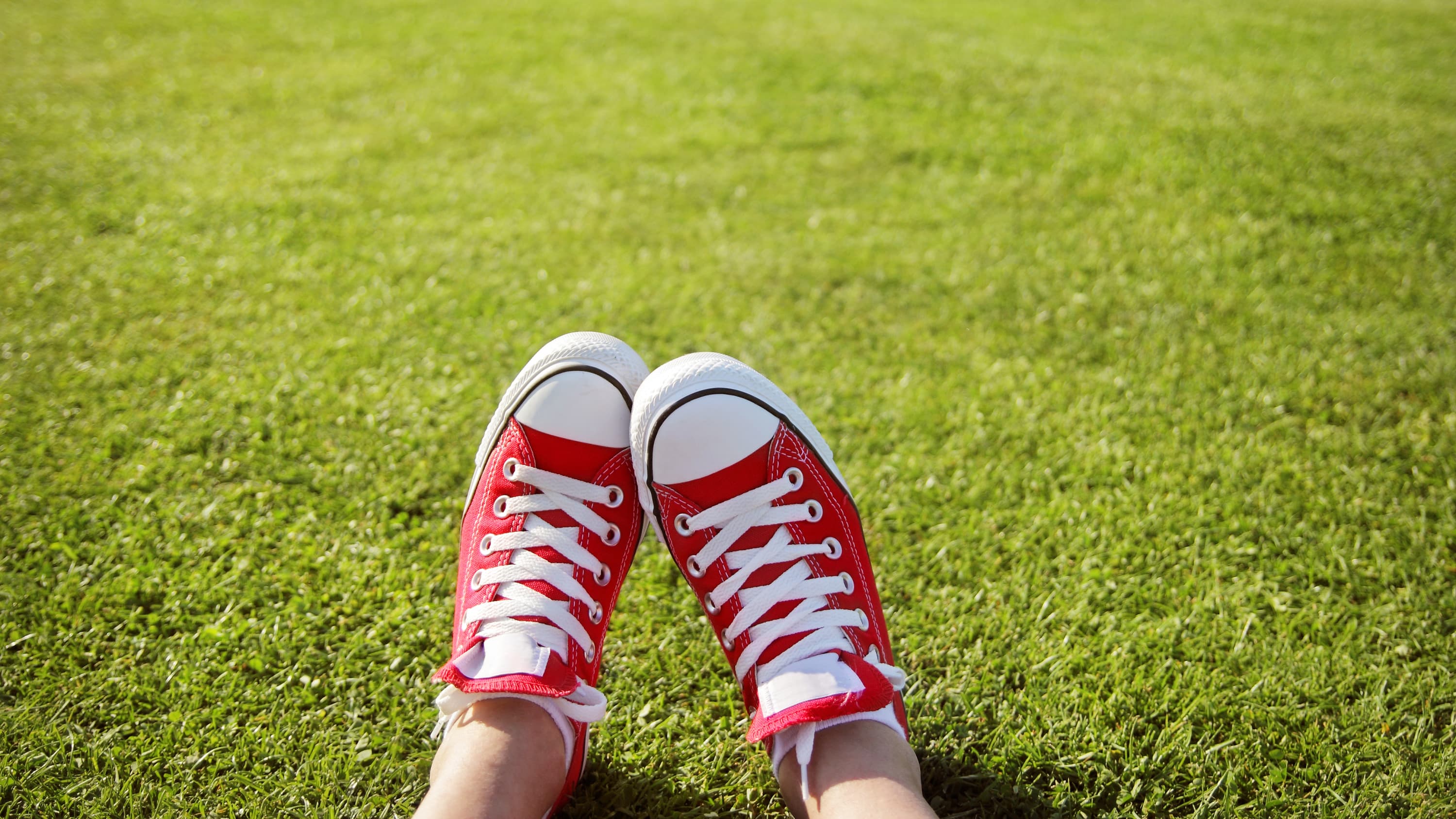a closeup of the feet (wearing sneakers) of a person, who has a limb leg discrepancy, sitting on the grass.