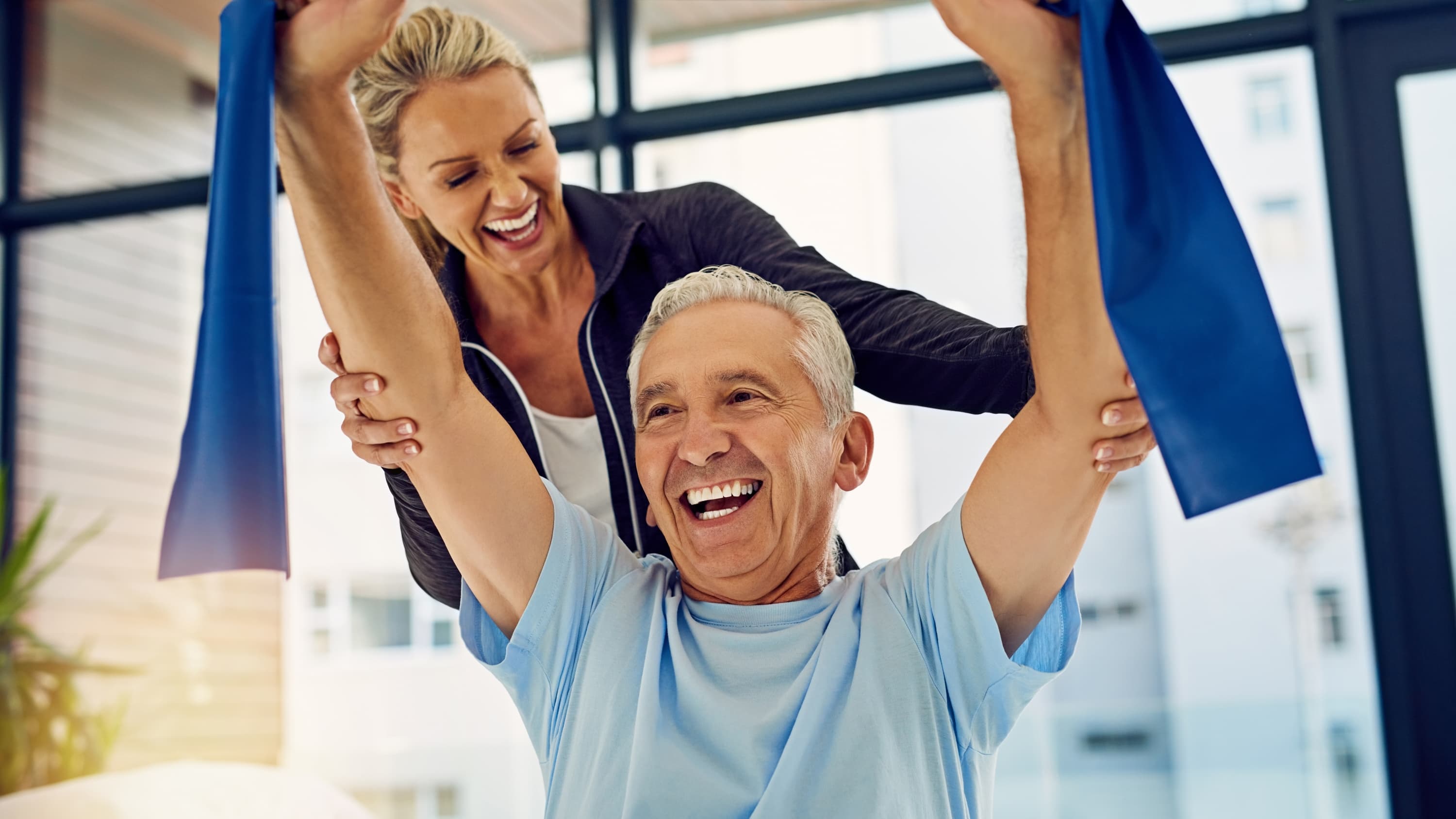 Photograph of a physical therapist helping a senior patient stretch with a stretch band in her office, possibly as part of cancer rehabilitation