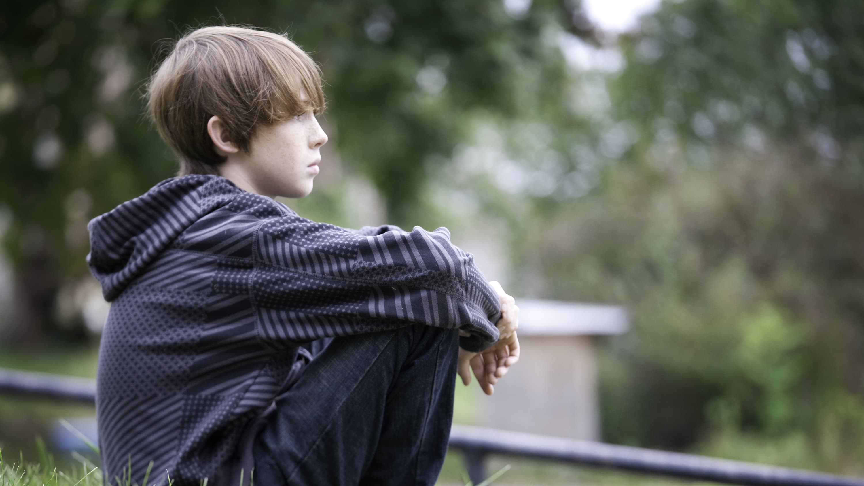 Photo of a young boy who may have stress and anxiety sitting contemplatively on the ground.