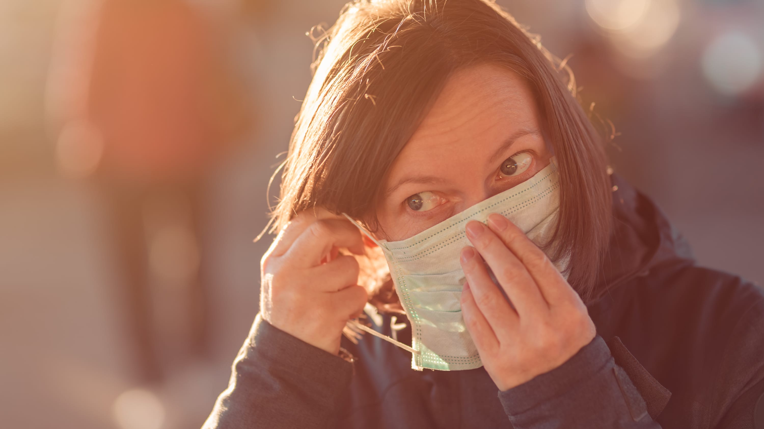 Woman with face protective mask standing on the street, possibly with post-COVID-19 symptoms