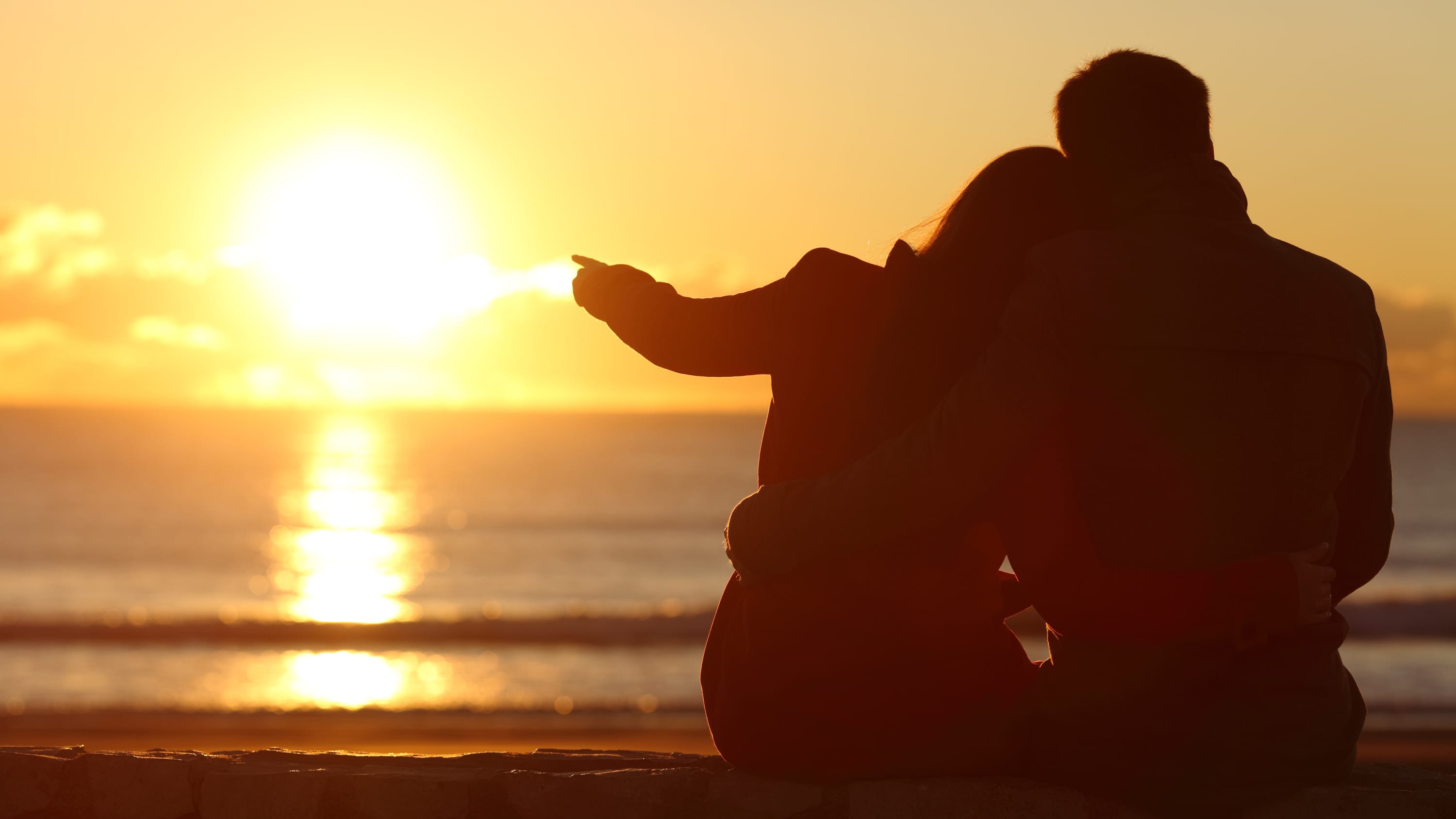 A man and woman sit on a beach and admire the sunset.