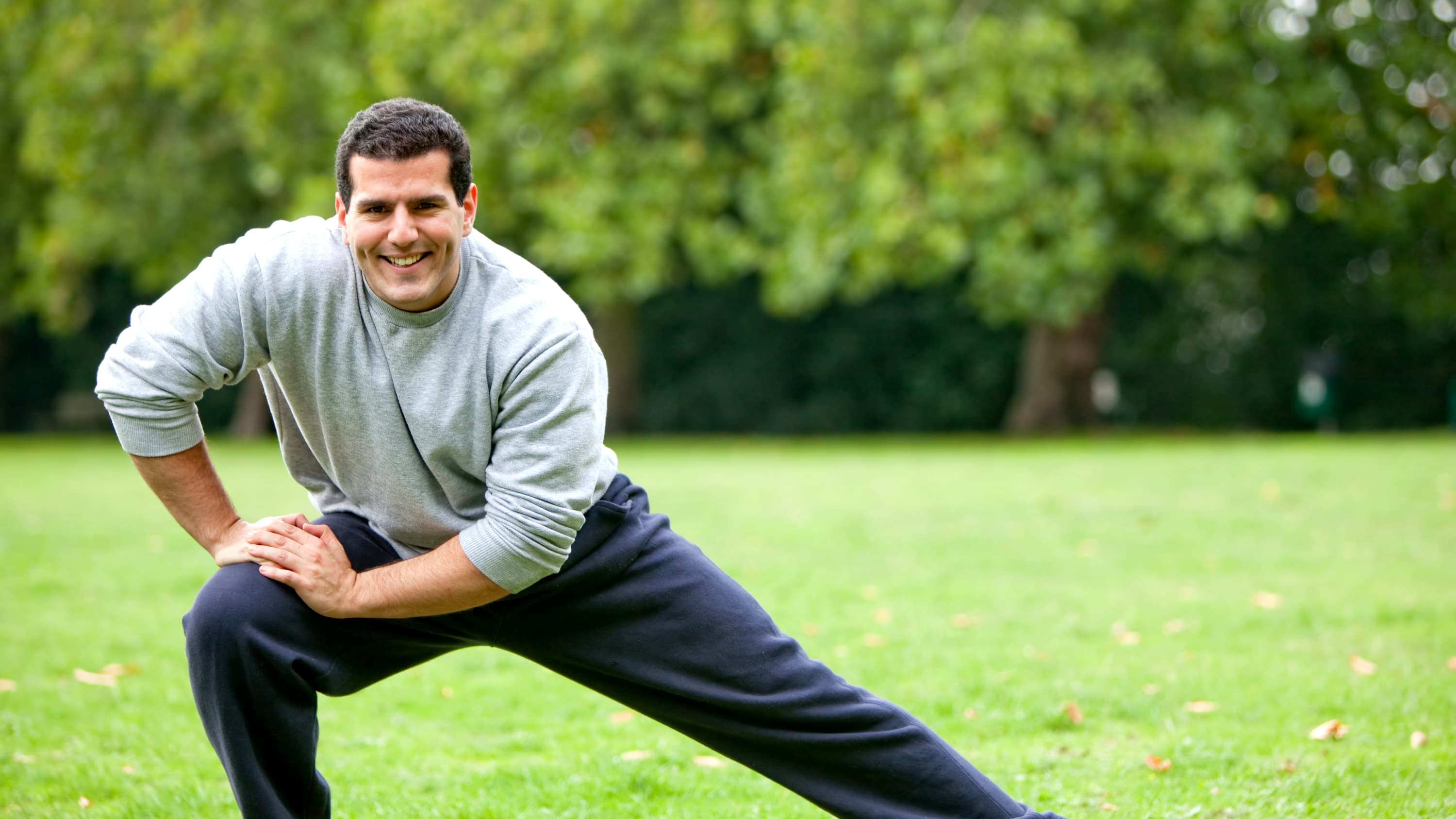 An athletic man in sweatpants who finally has pain relief after surgery stretches in the park.