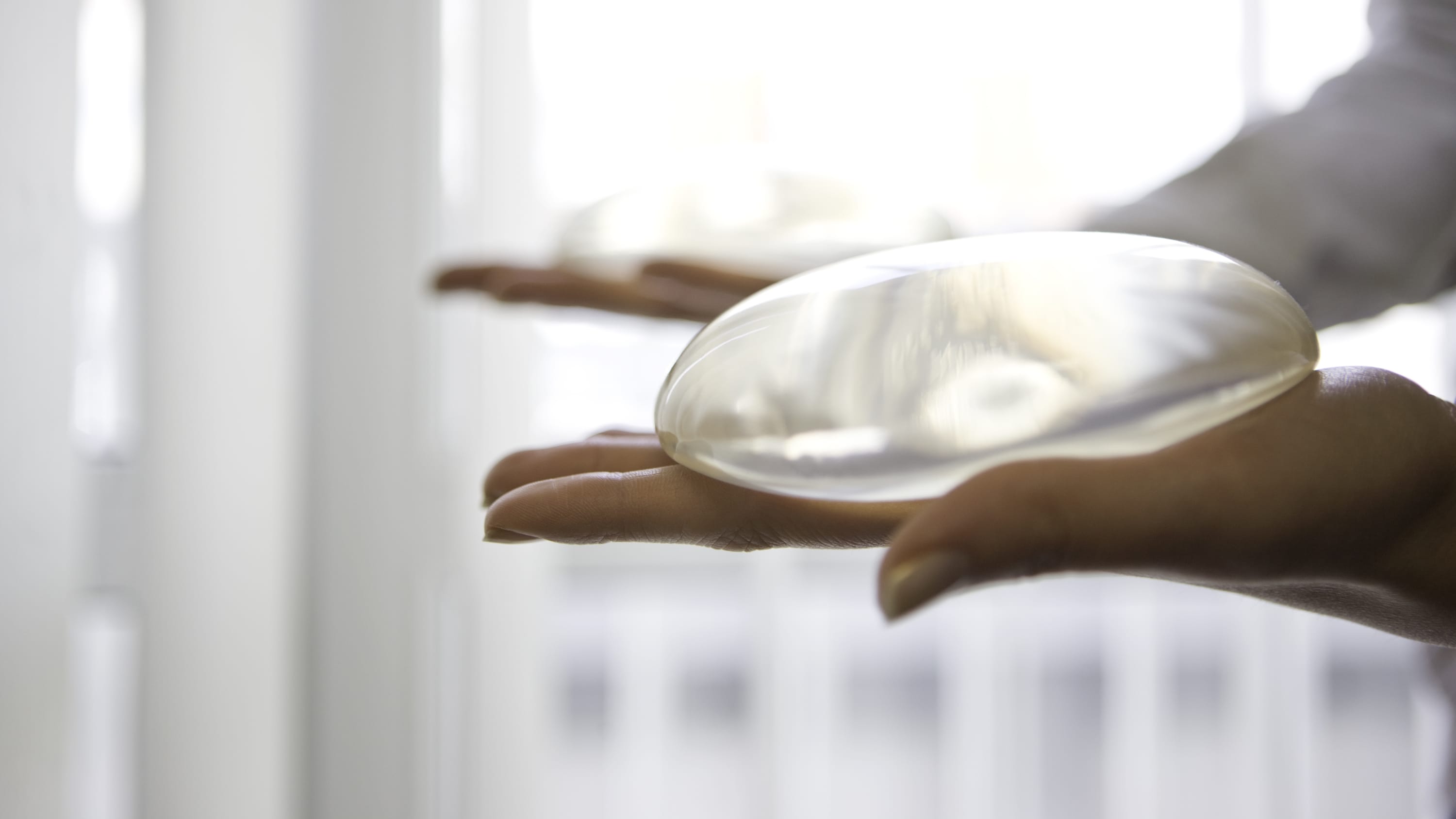 Hands holding a round, silicone breast implant.