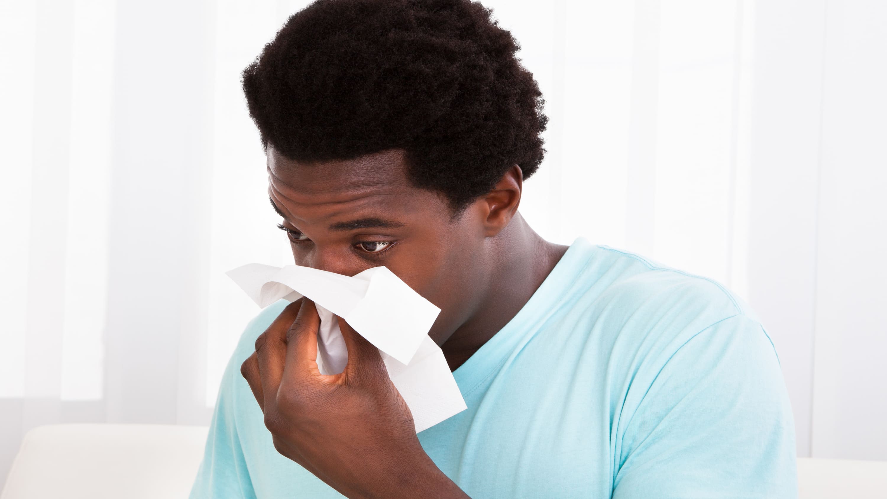A man suffering from a cold blows his nose.