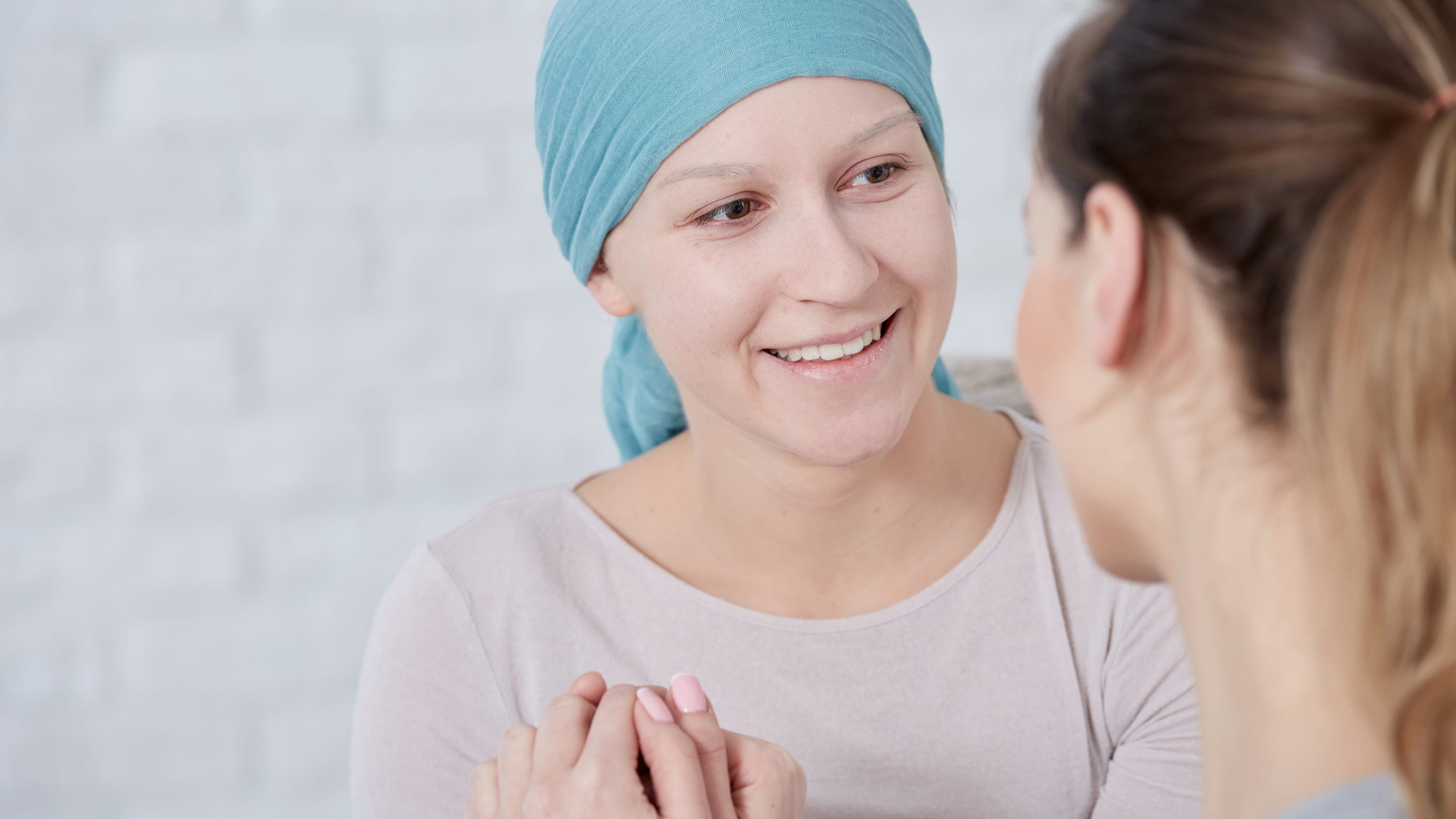 A woman in a head wrap smiles as she converses with a woman with a pony tail.