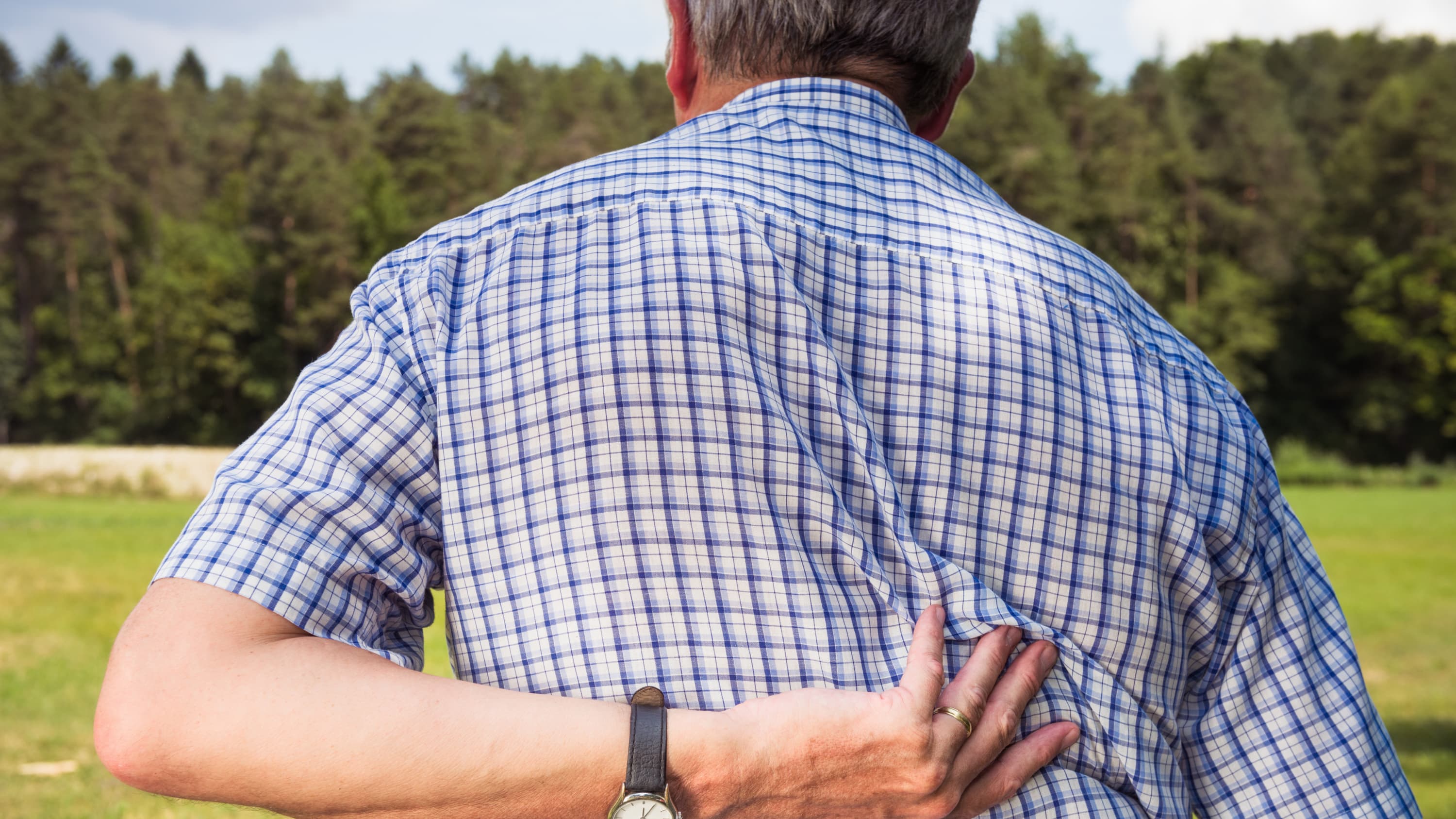 A man with a degenerative and rheumatologic spinal disorder presses his hand against his back.