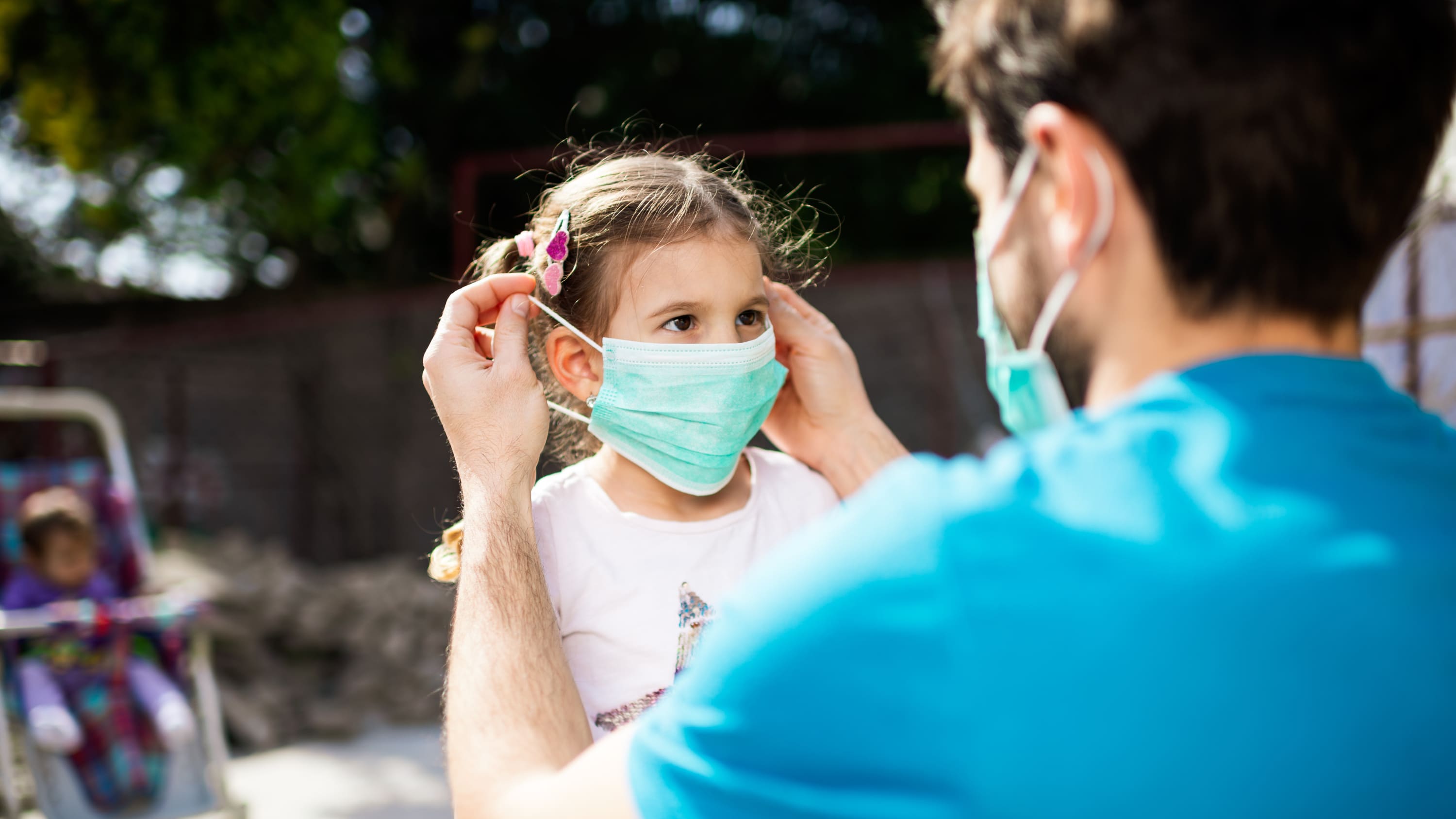 father putting mask on his daughter, possibly to protect against covid-19-related PMIS