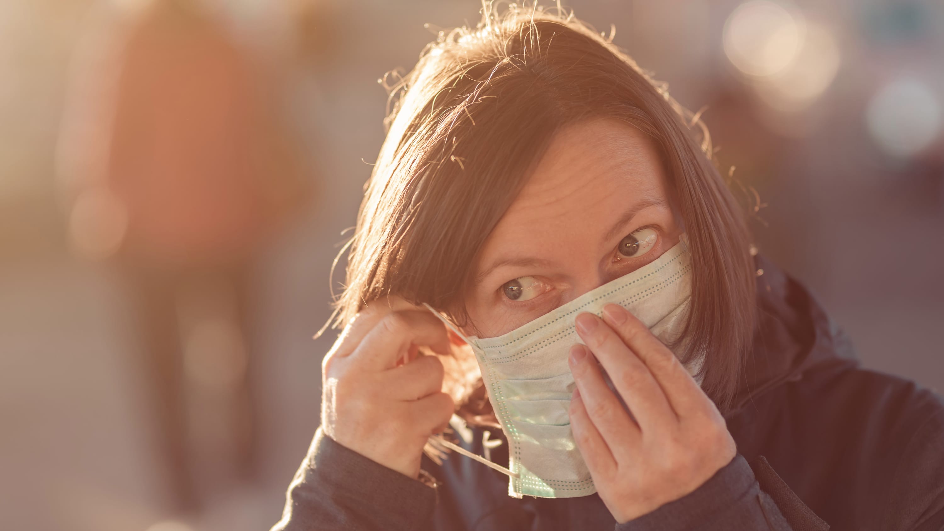 Woman with face protective mask standing on the street, possibly with post-COVID-19 symptoms