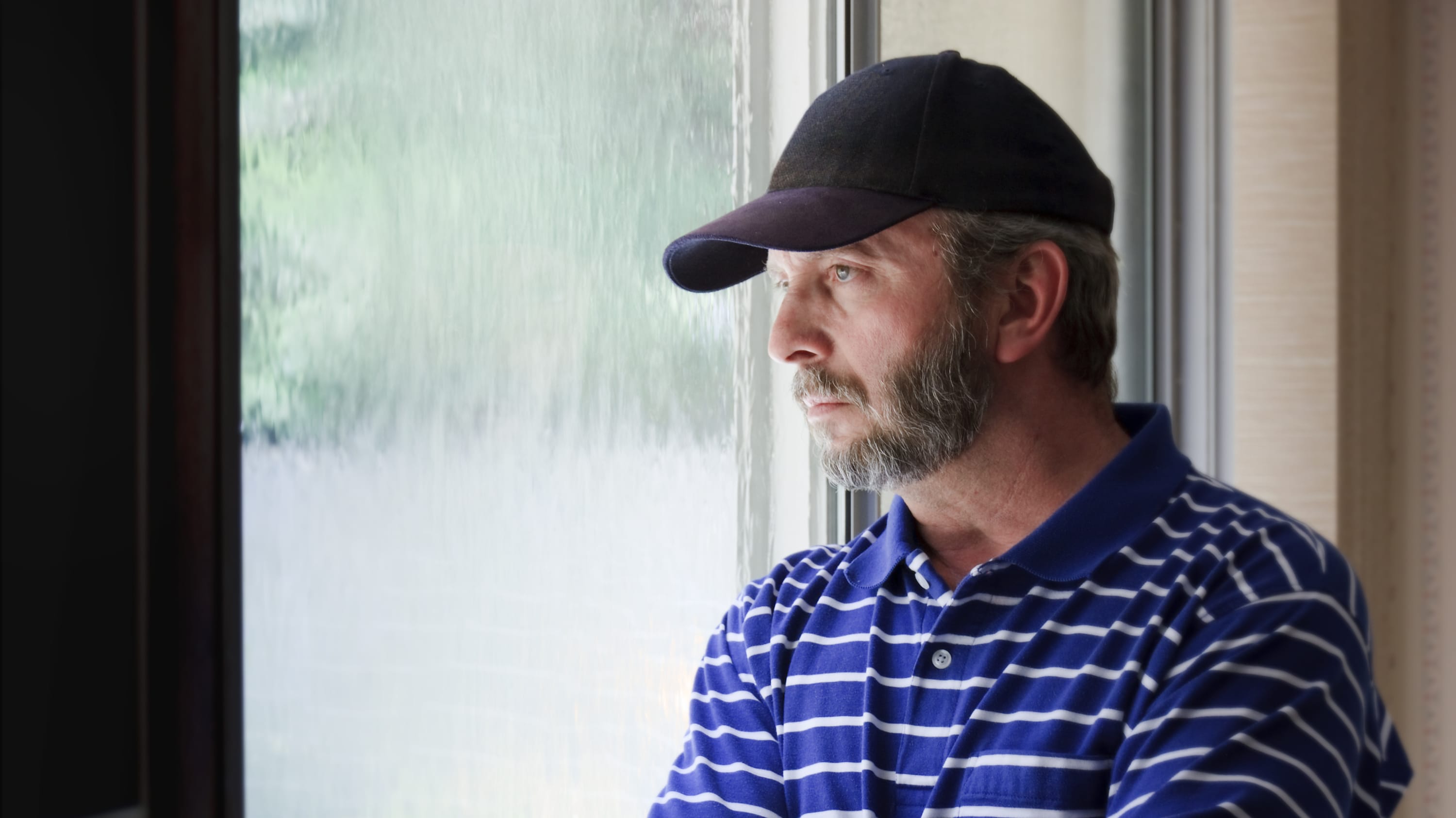 Adult male looking out a rain covered window looking concerned, possibly about a gambling disorder
