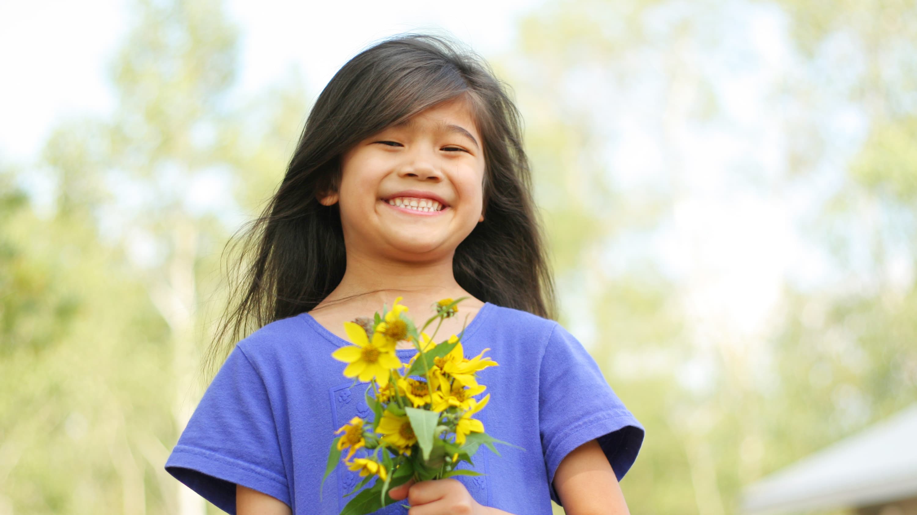 A young girl with epilepsy smiles for the camera while holding flowers.