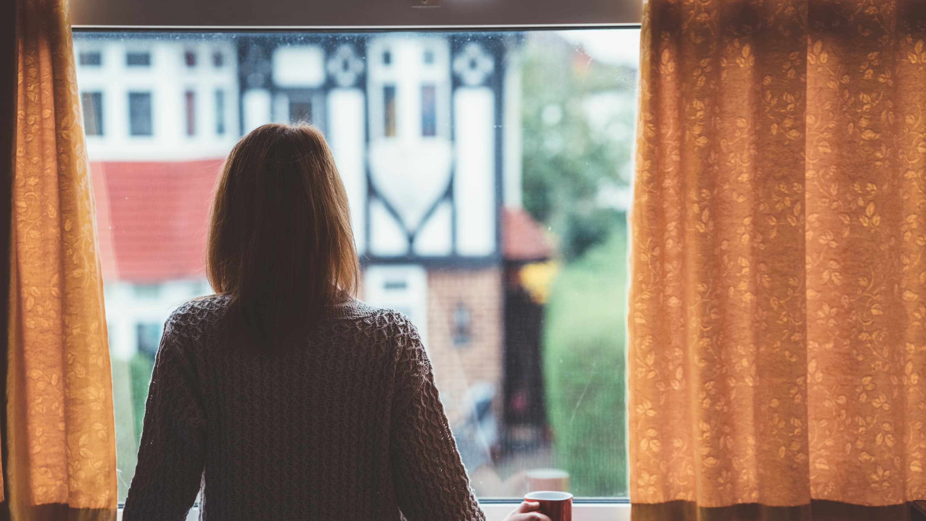 woman looking out a window, dealing with social isolation from COVID-19