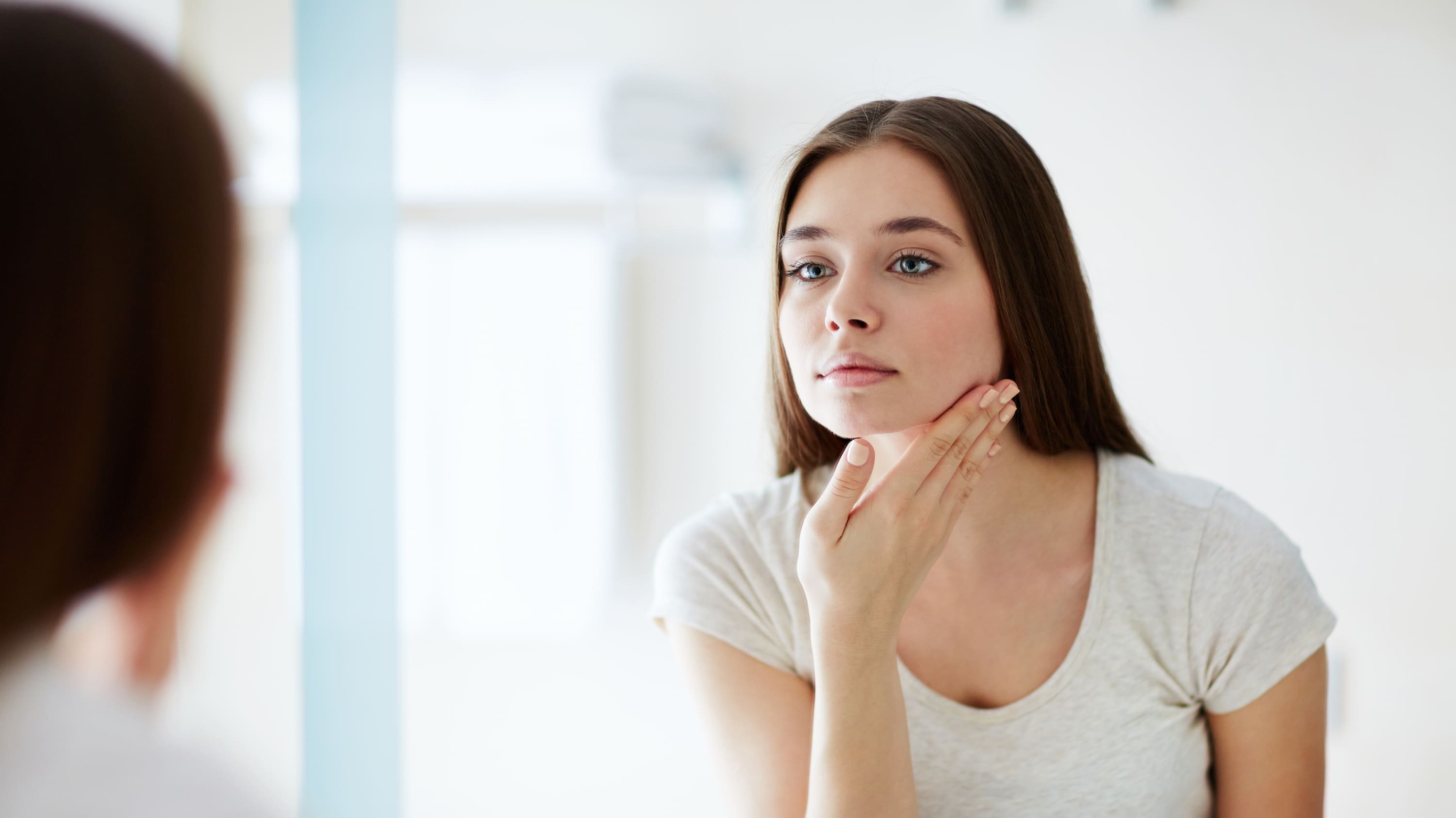 woman looking into a mirror, possibly considering at-home beauty products