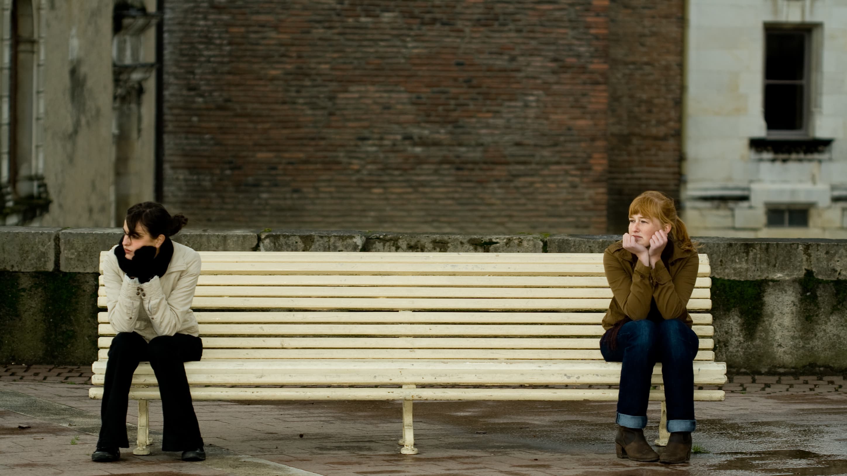 two girls on opposite sides of a bench, practicing social distancing during COVID-19 pandemic