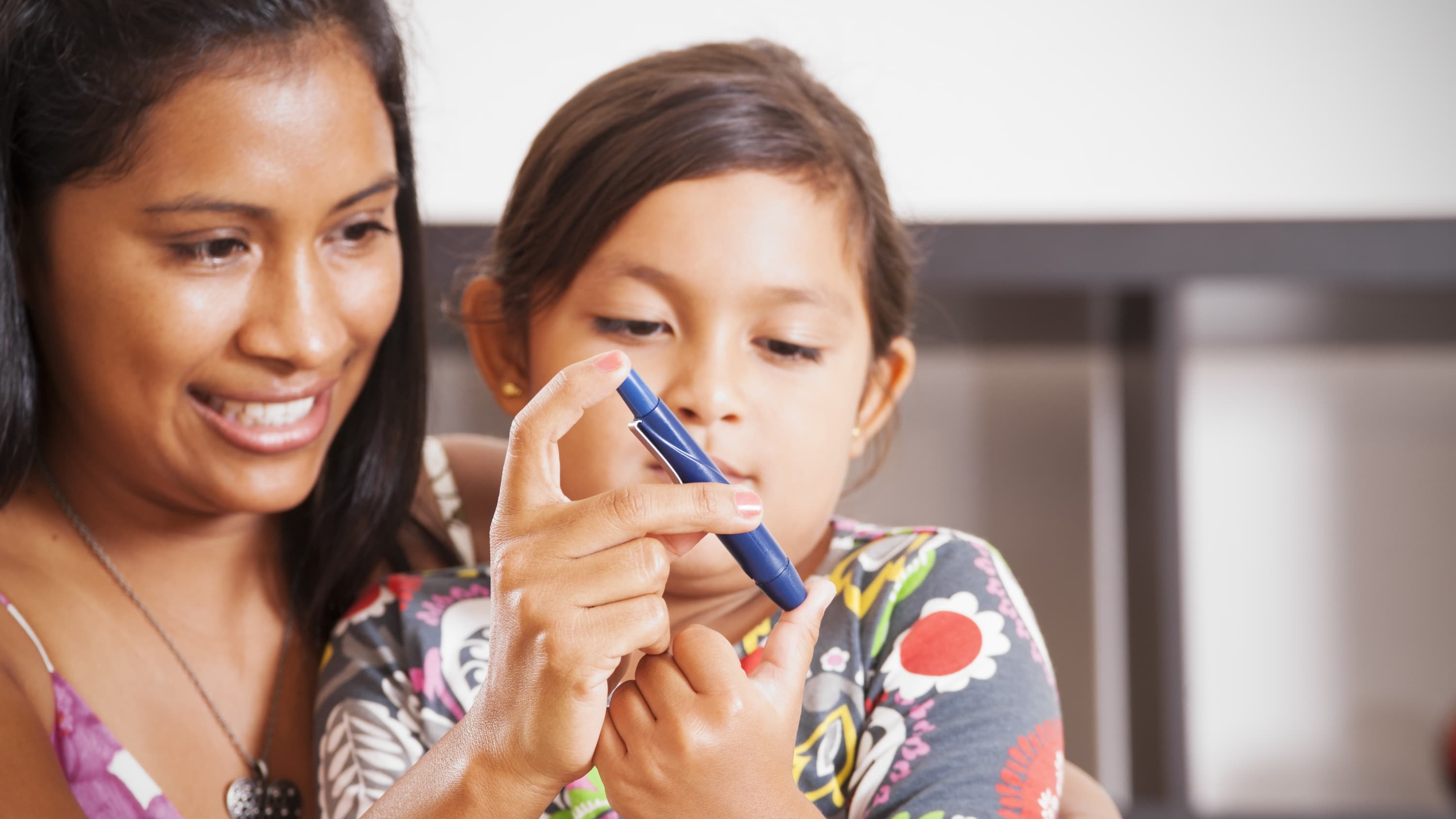 A mother helps her young daughter use a device to test blood sugar in people with diabetes