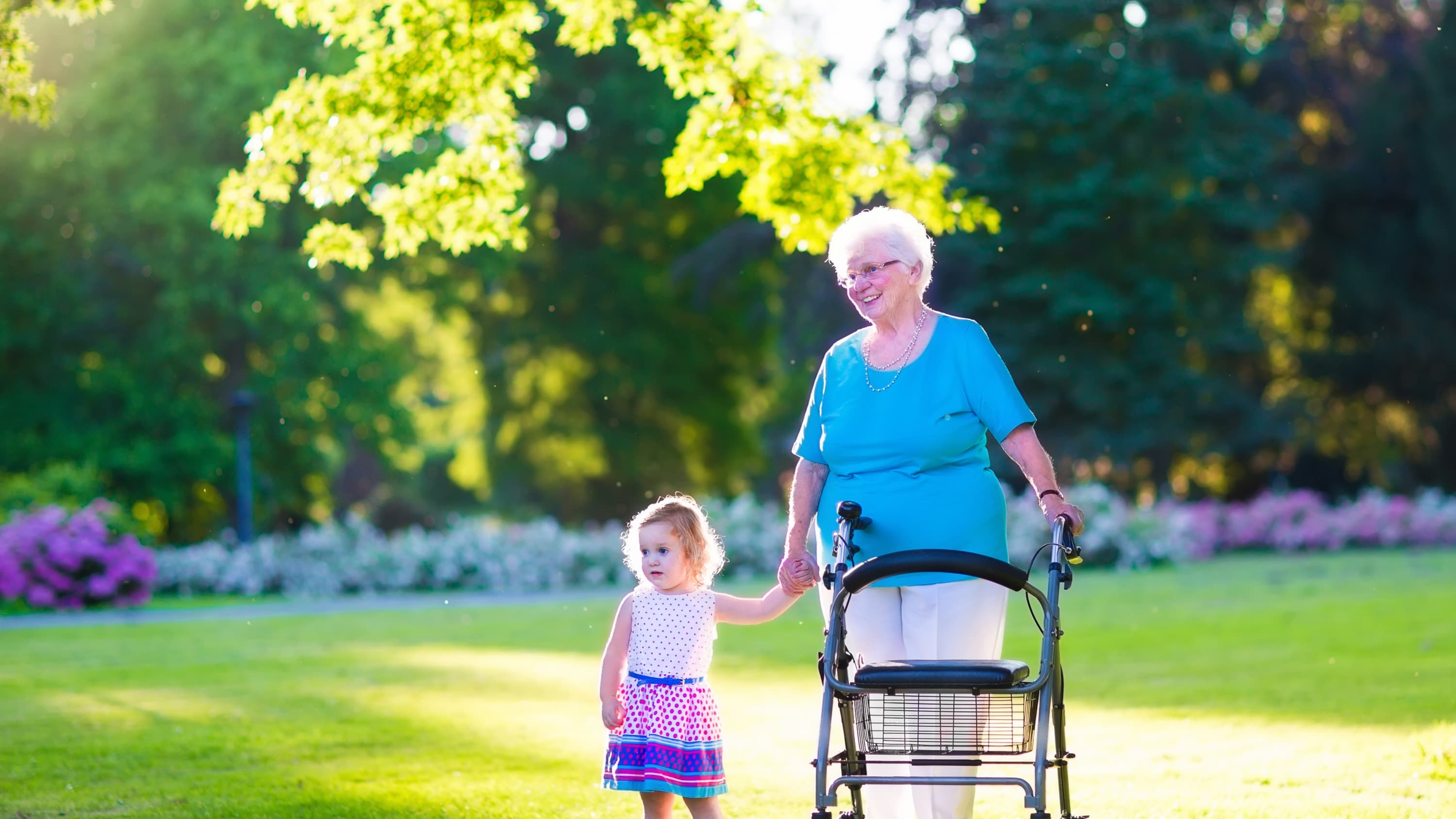 Happy senior lady with a walker or wheel chair and a little girl walk in a park, possibly after the woman had a hip fracture