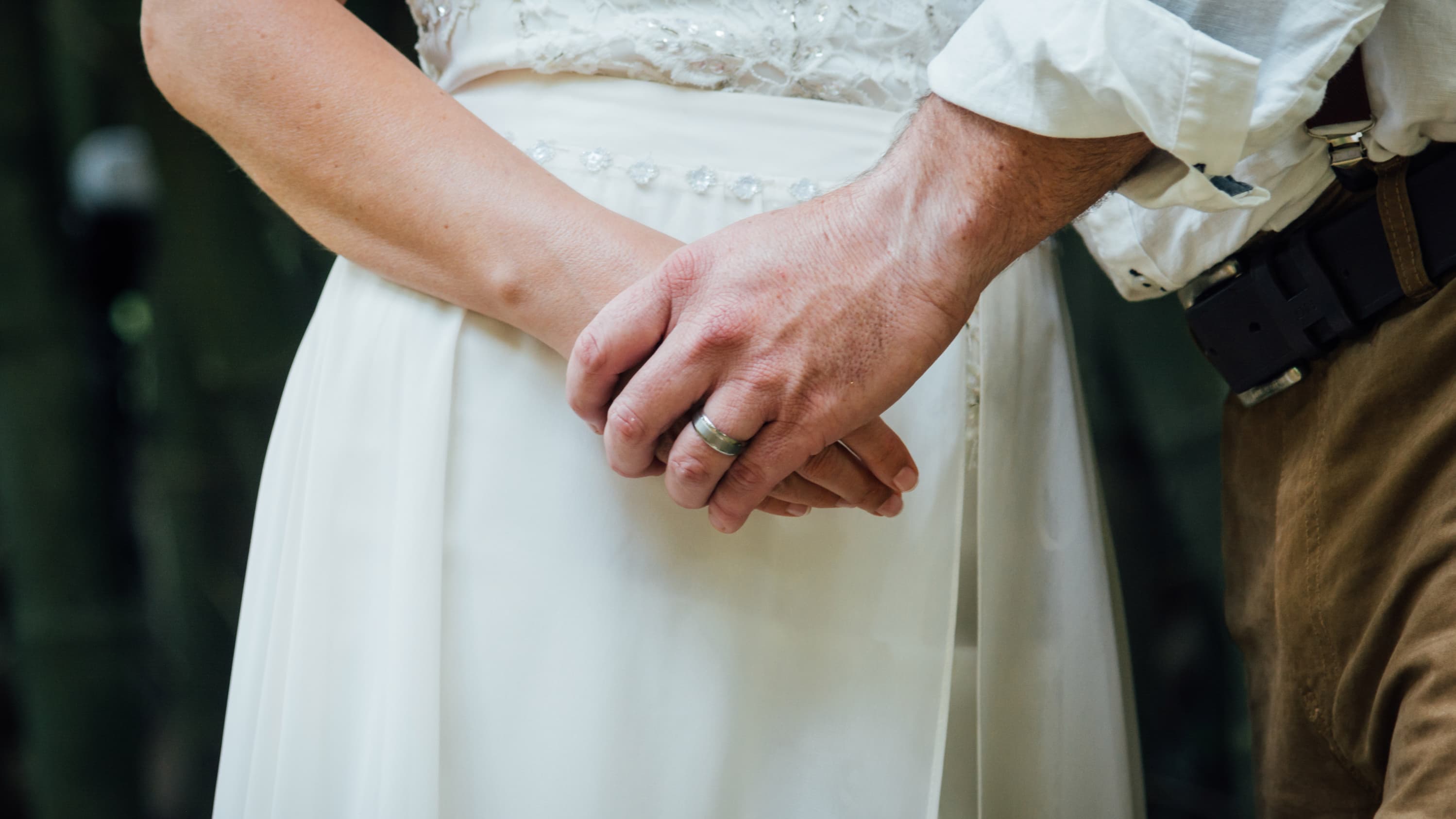 A newly married couple hold hands, closeup is on the hands.