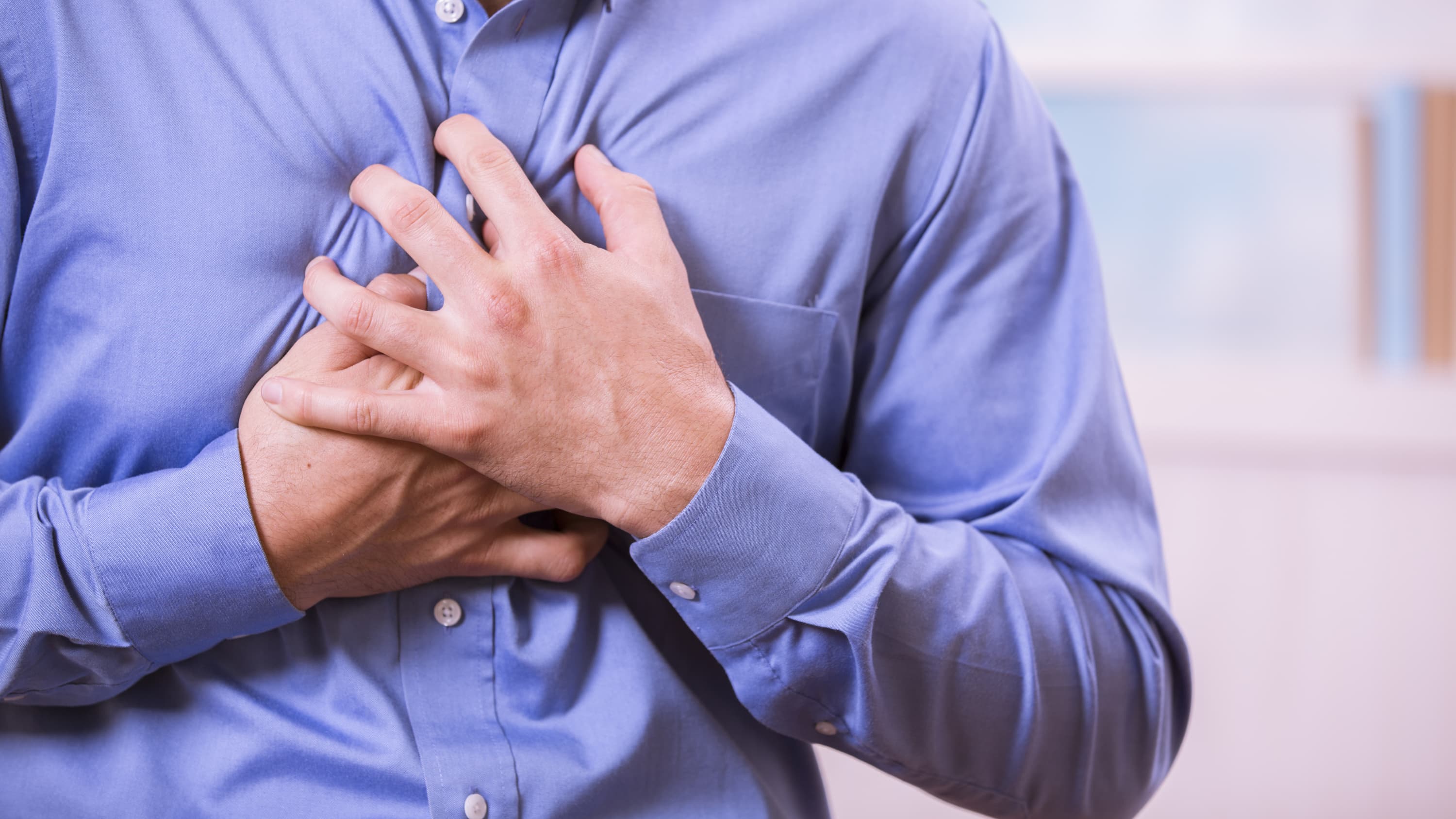 A man in a blue shirt who may have a pulmonary embolism clutches his chest.