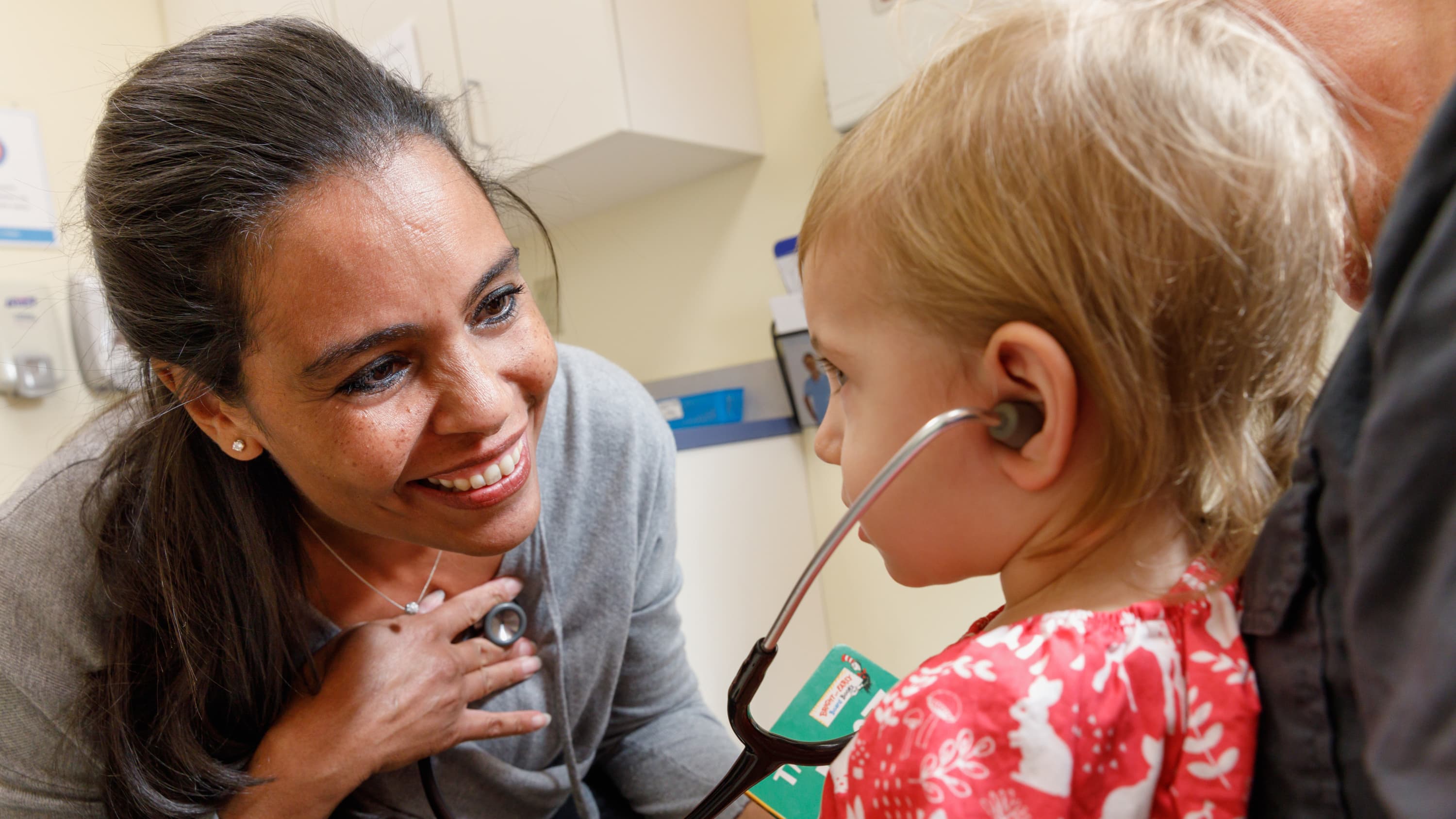 Dr. Annette Cameron is making a young patient feel comfortable by having her listen to her heartbeat using a stethoscope.