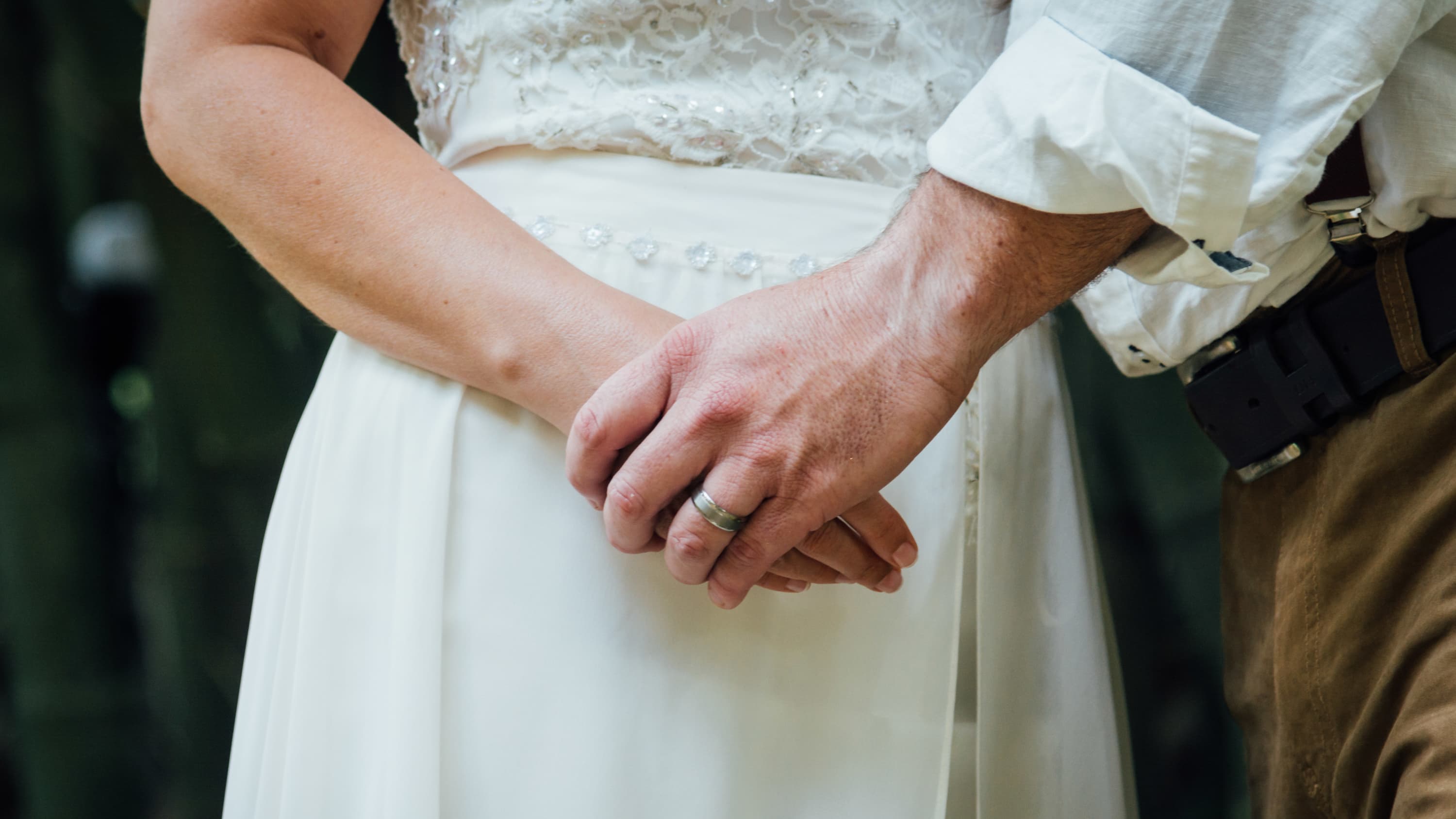 A newly married couple hold hands, closeup is on the hands.
