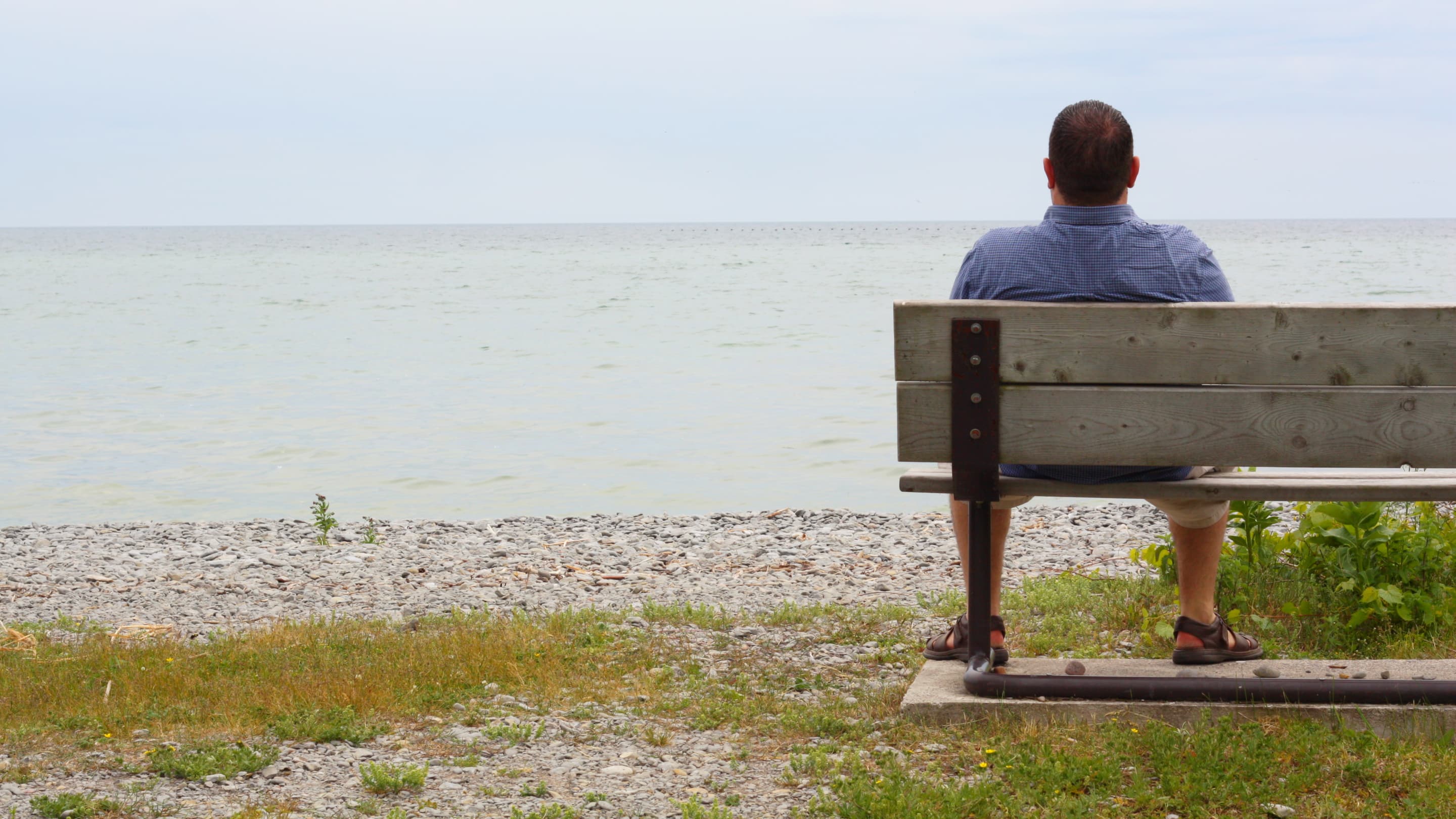 A man coping with heart failure sits on a bench at the beach looking out at the water.
