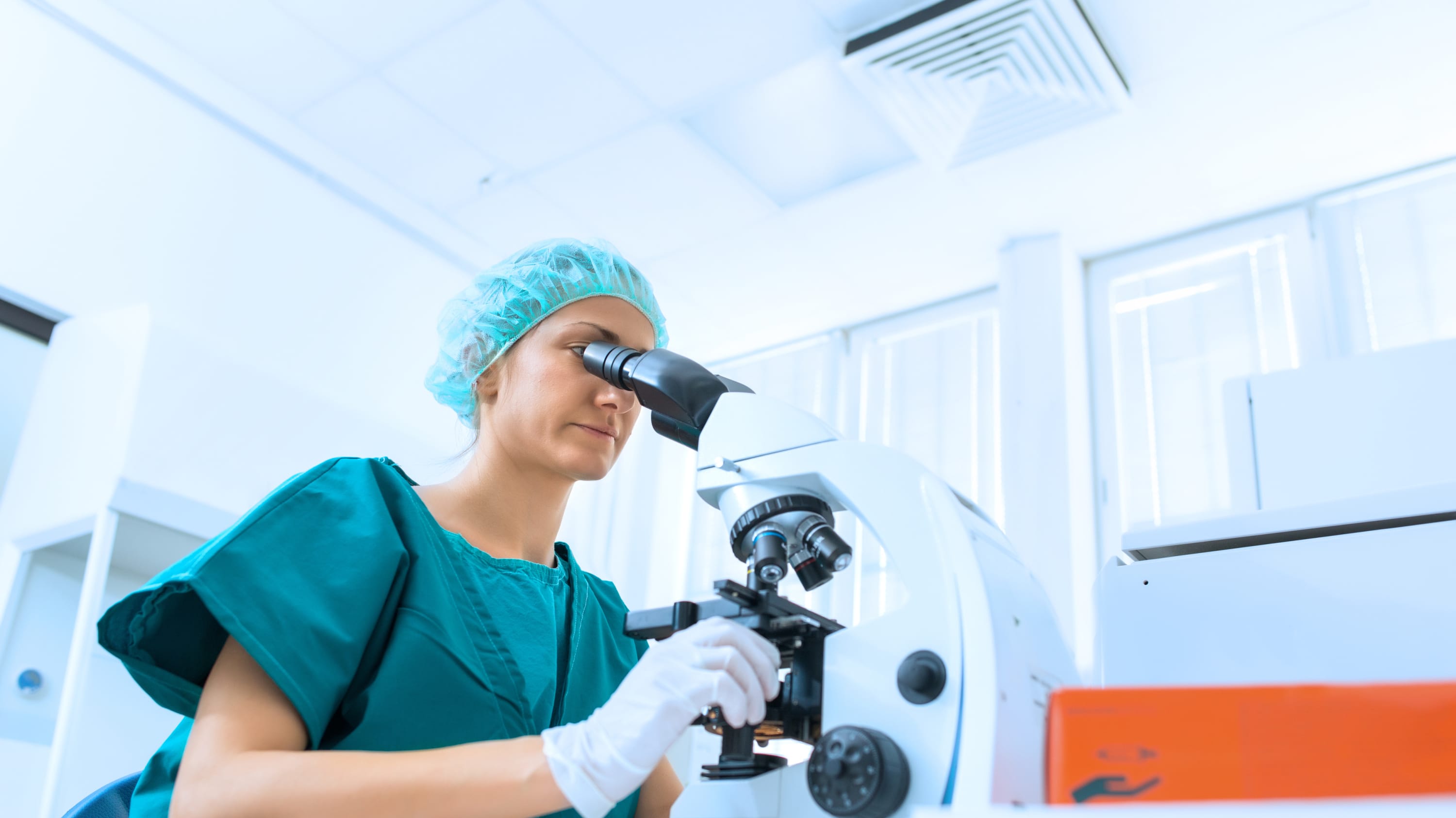 A lab technician looks into a microscope, possibly examining semen in a patient with male infertility.
