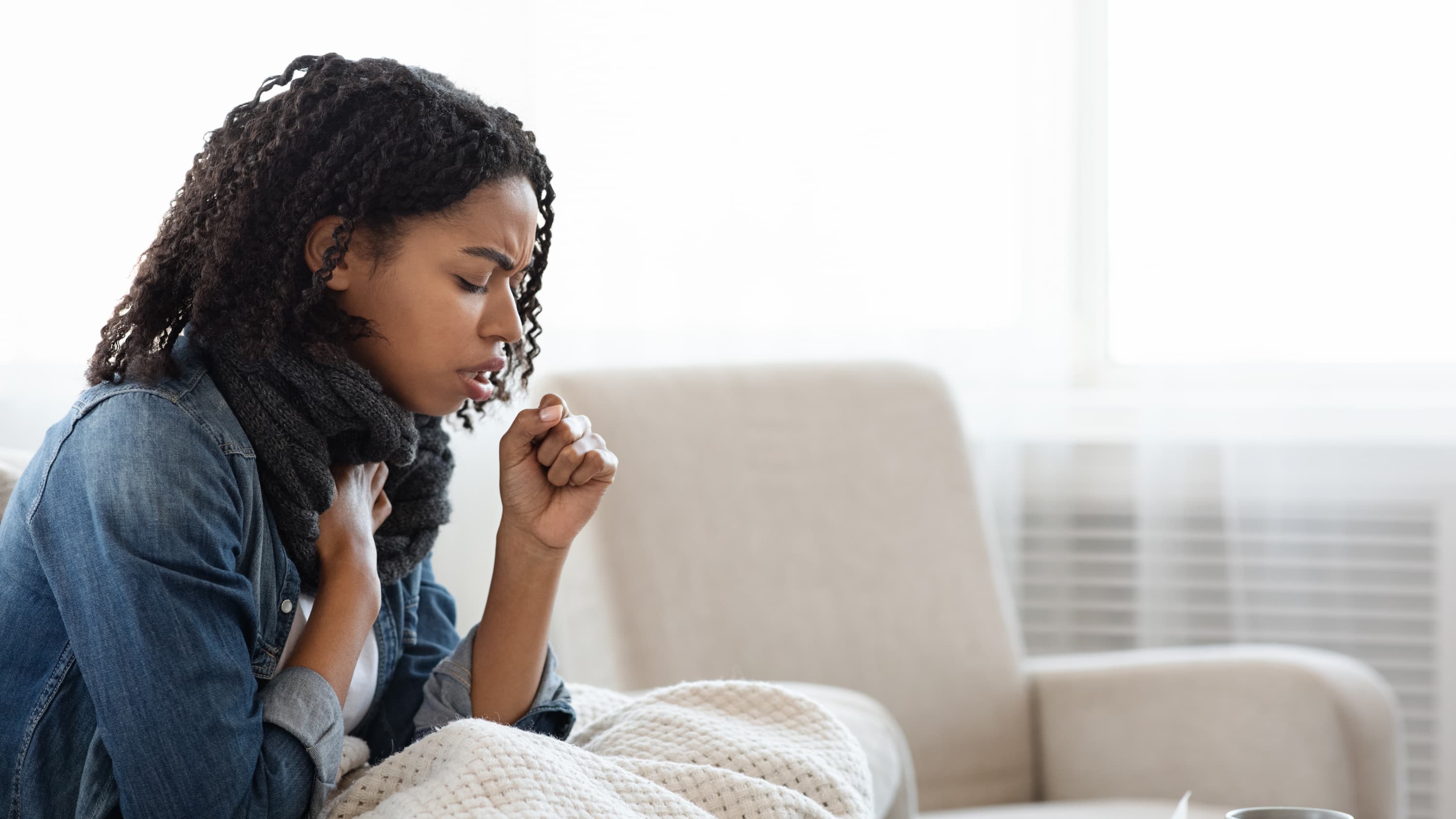 young woman with walking pneumonia on a couch coughing