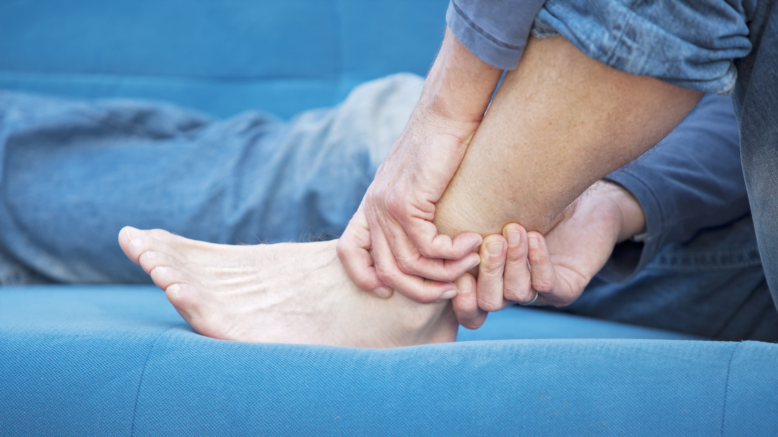 A man with lupus nephritis gripping his ankle on a blue couch.