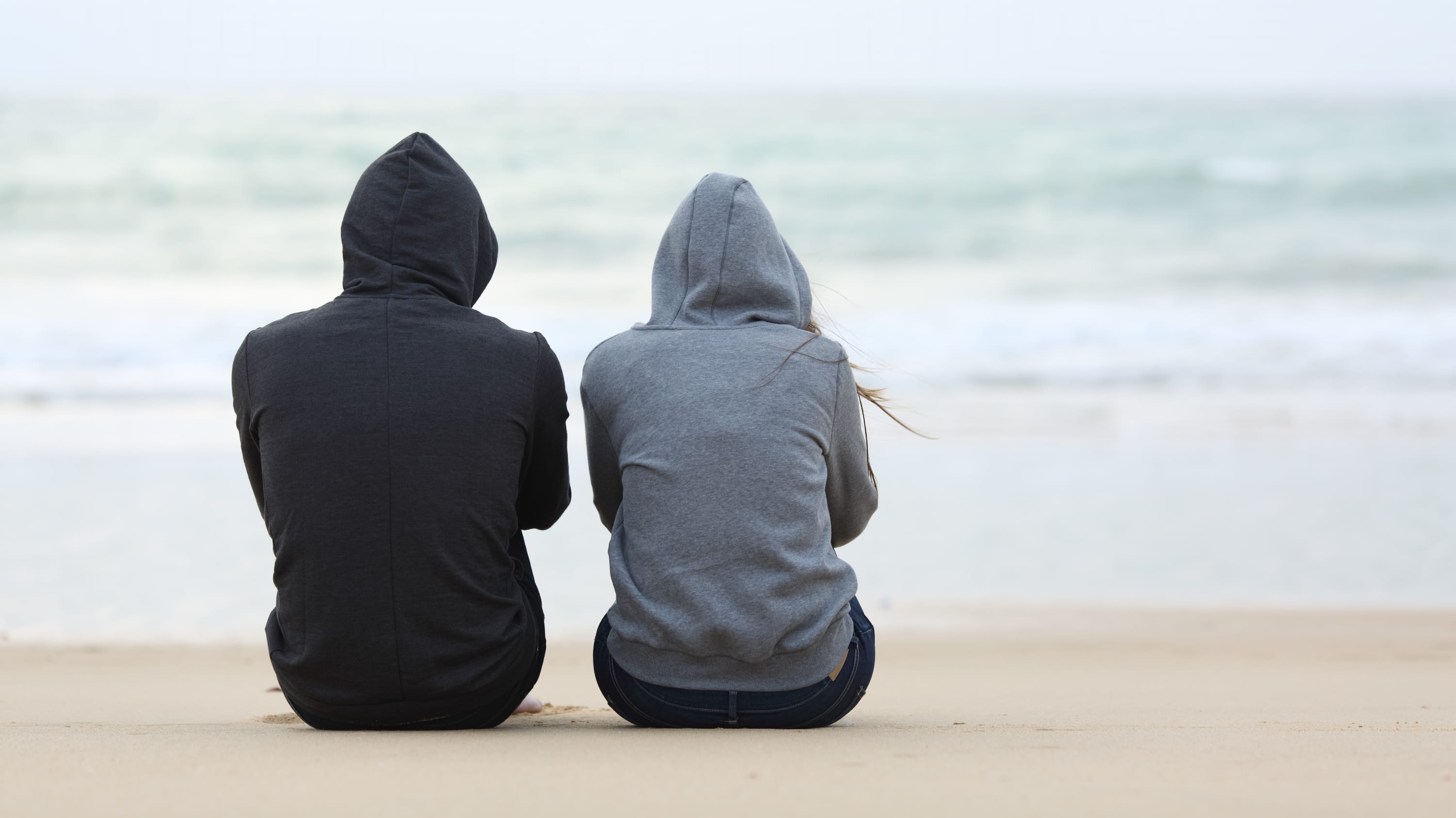 A man and a woman sit on a beach, possibly talking about herpes