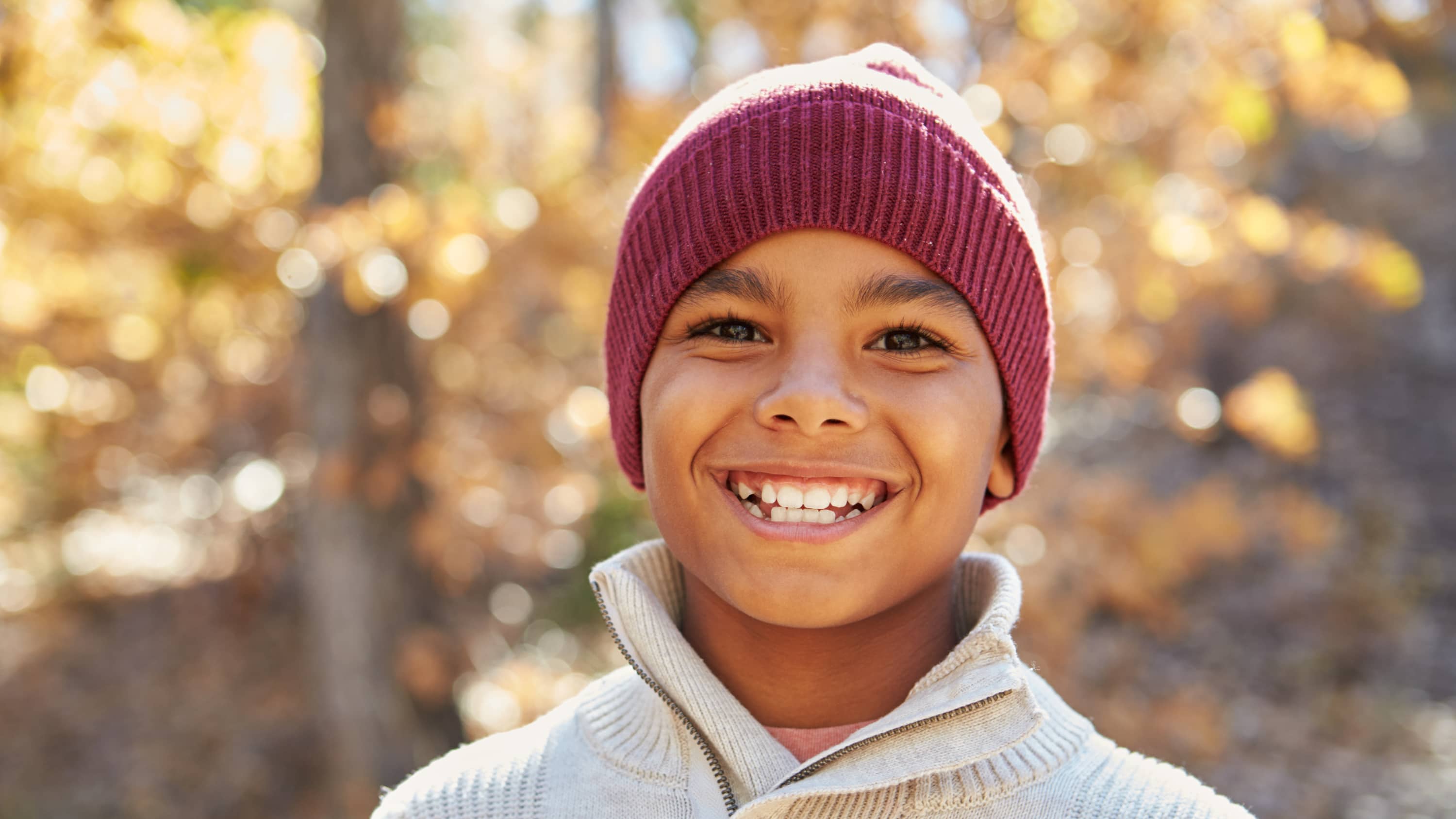 Boy who may have ADHD stands outside with a hat on, smiling.