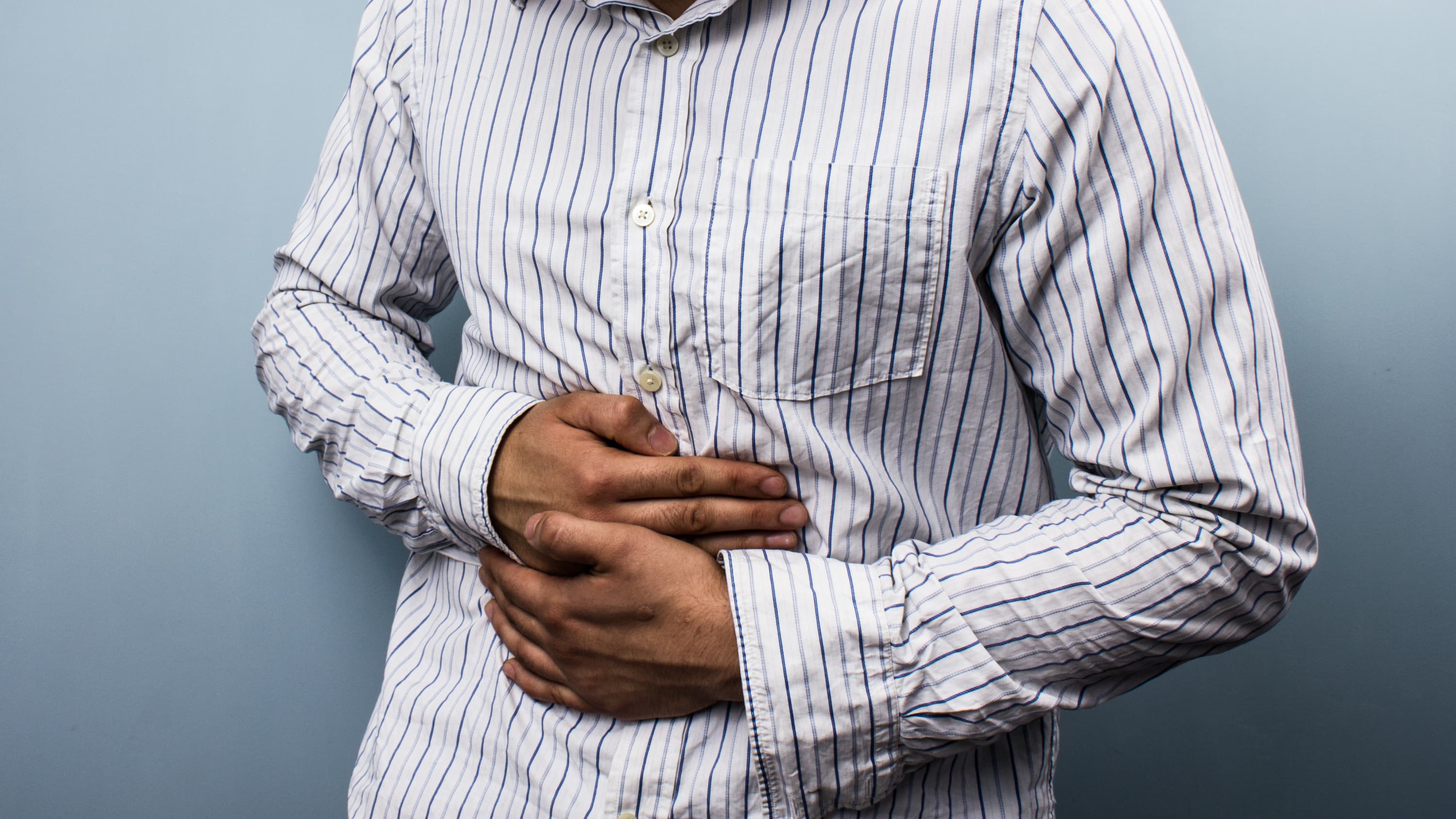 Man holds stomach in discomfort, he is suffering from ulcerative colitis.