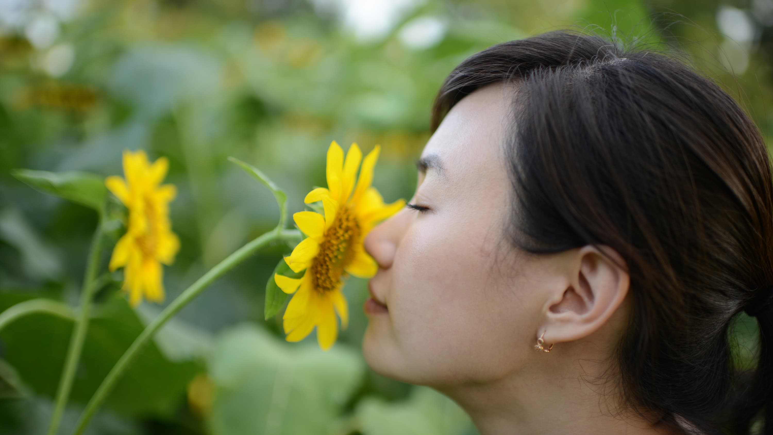 A woman who is trying to (but cannot) smell the flowers because of anosmia.