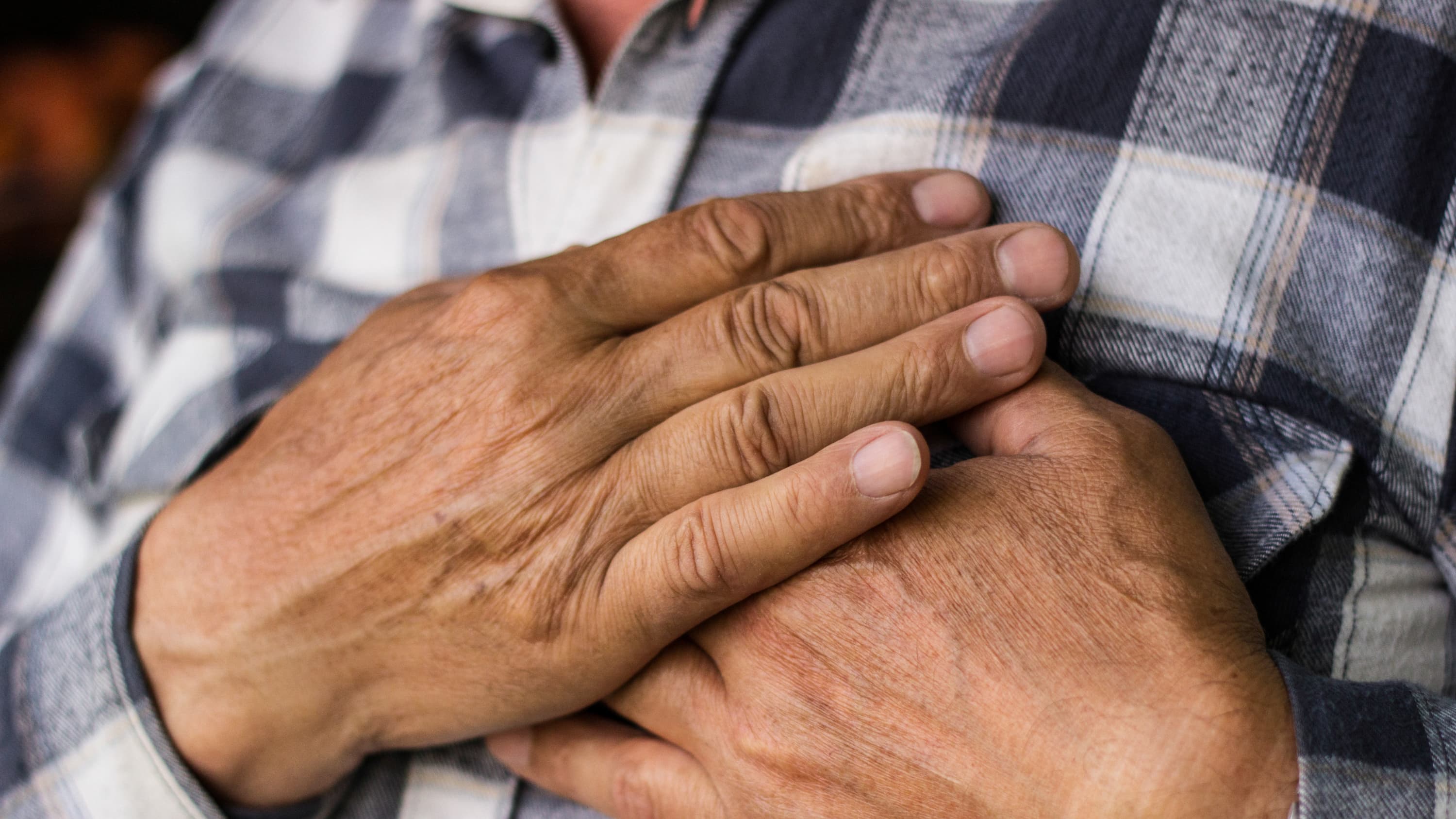 An elderly man clutches his chest in response to pain that could be a sign of a heart attack.