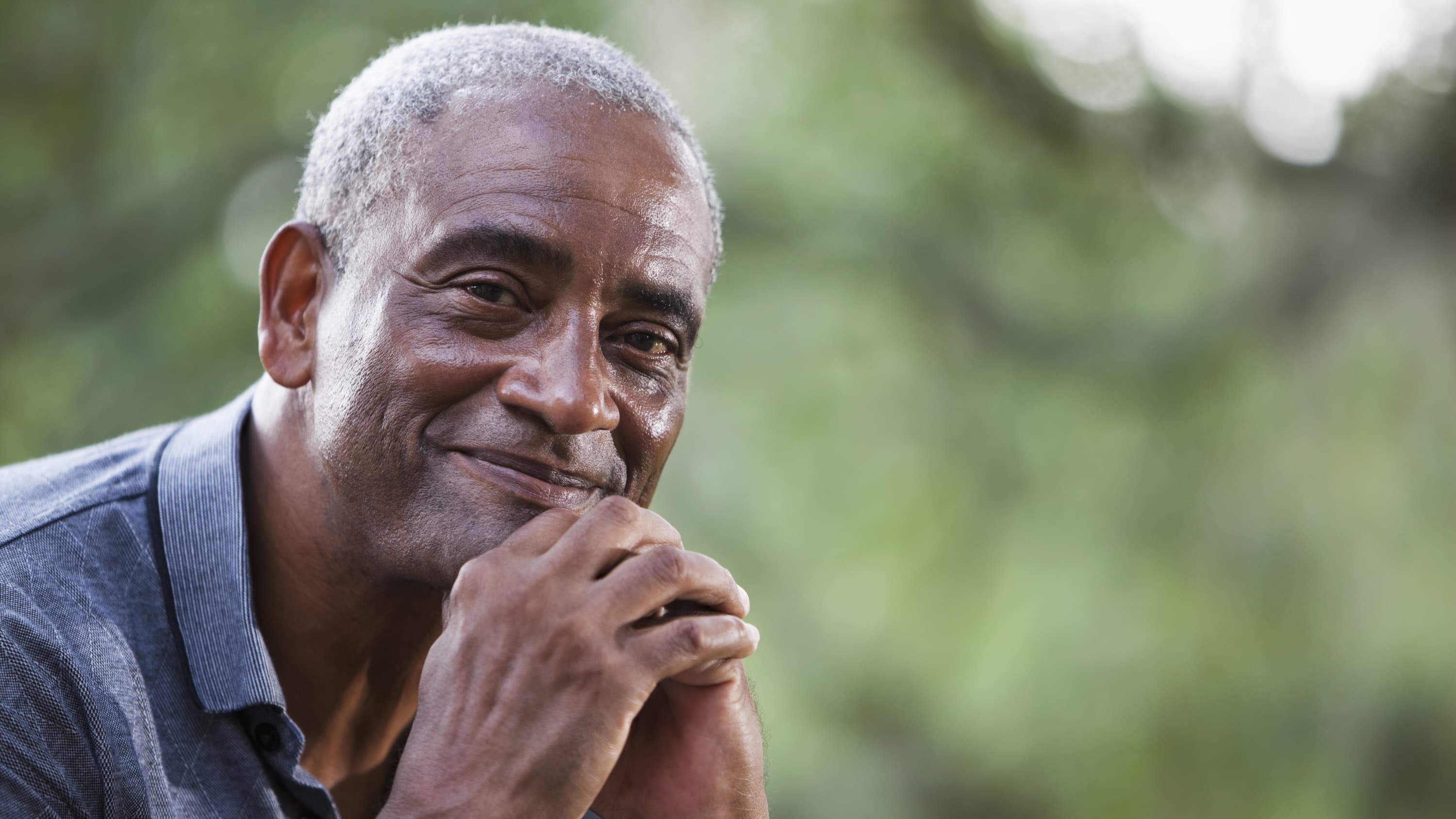 An older man who is holding his hands in front of his face and may be smiling because he had a negative prostate cancer screening .