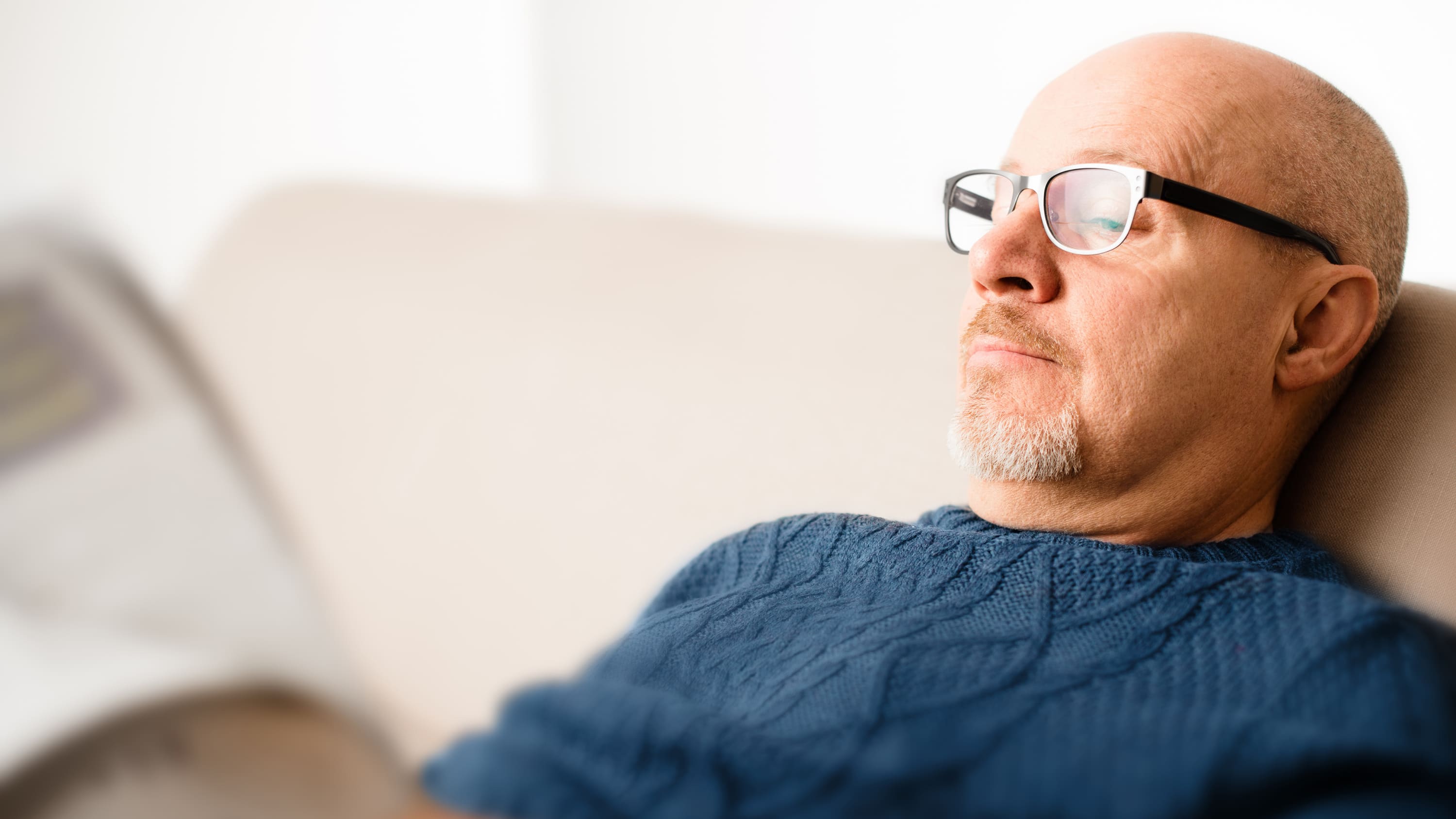 Middle-aged man who could be a candidate for peripheral vascular disease sits on the couch reading a newspaper.