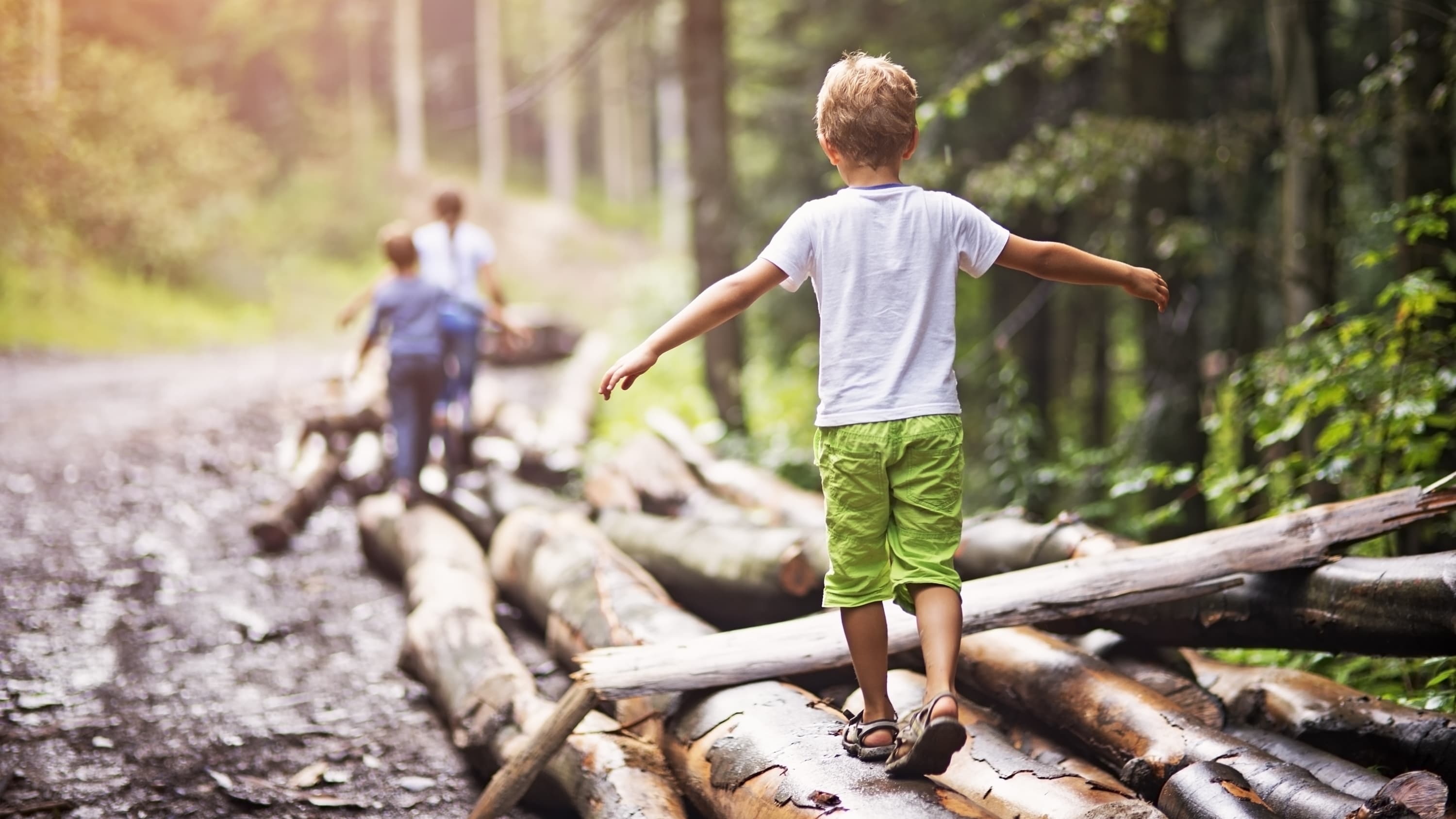 Children who might have juvenile idiopathic arthritis try to balance as they walk across some logs in the woods.