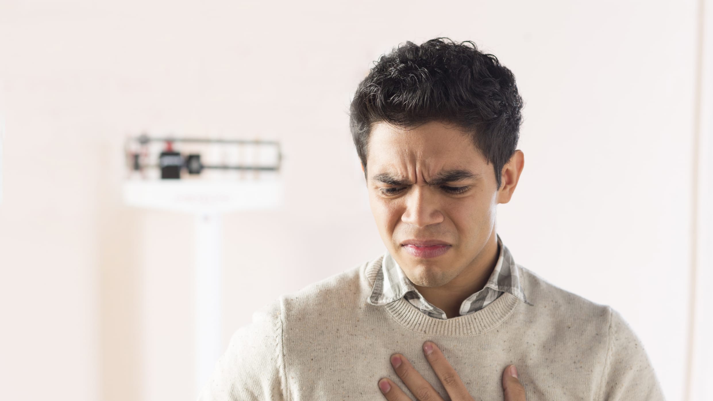 A young man experiencing dysphagia stands in an exam room holding his chest.
