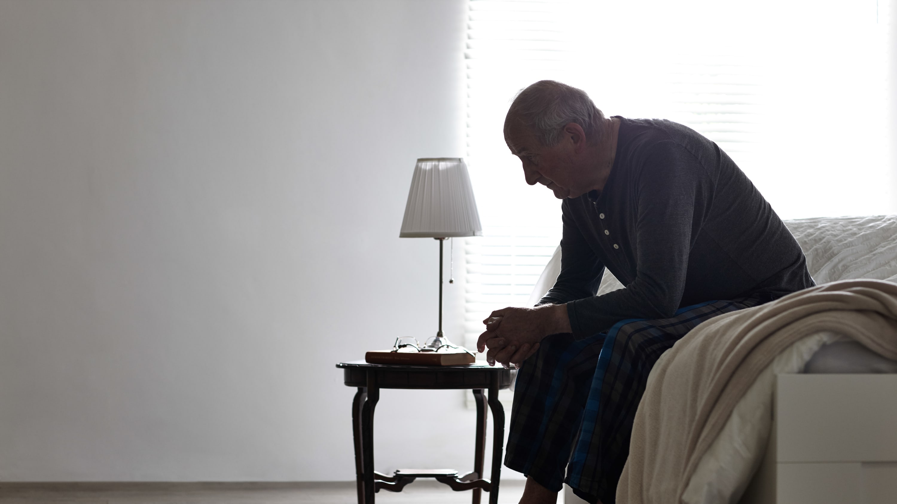 An older man with congestive heart failure sits on the edge of his bed feeling exhausted.