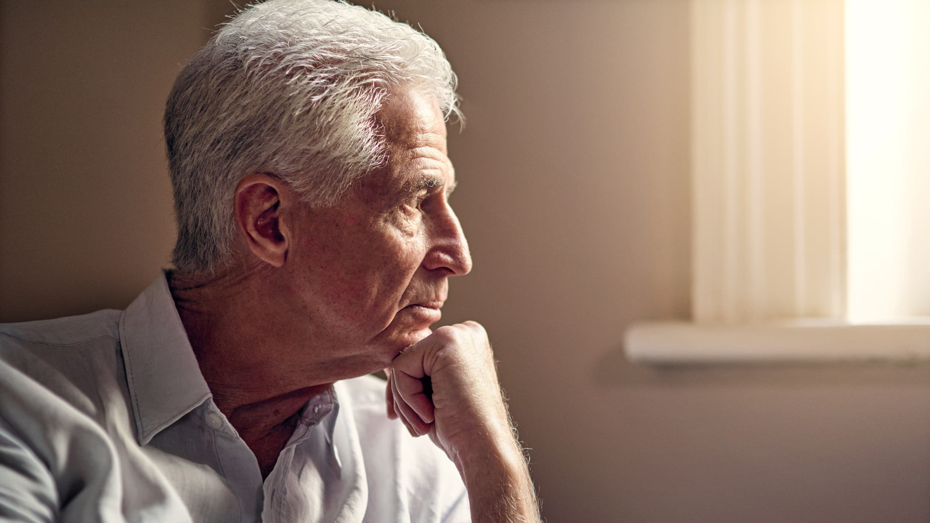 An elderly gentlemen looks out a window, who may be worried about pancreatic cancer.