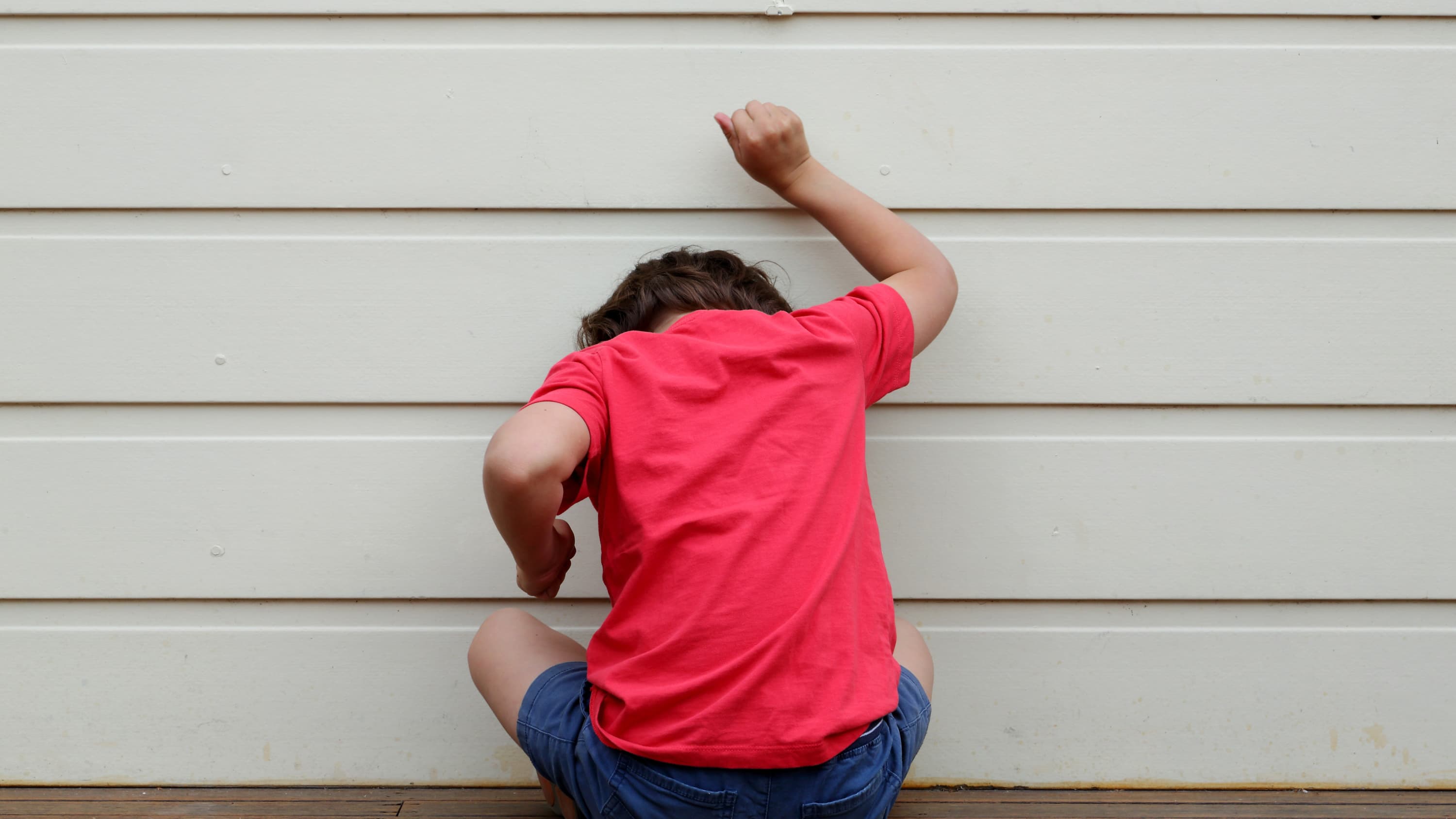 A child in a pink shirt who may have oppositional defiant disorder bangs on a wall.