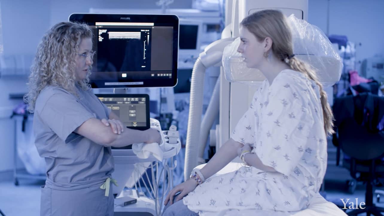 Yale interventional radiologist Dr. Bass talks to a patient in a procedure room.