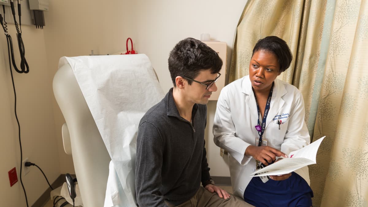 Doctor sits beside a patient in an exam room talking about a possible thyroid cancer diagnosis.