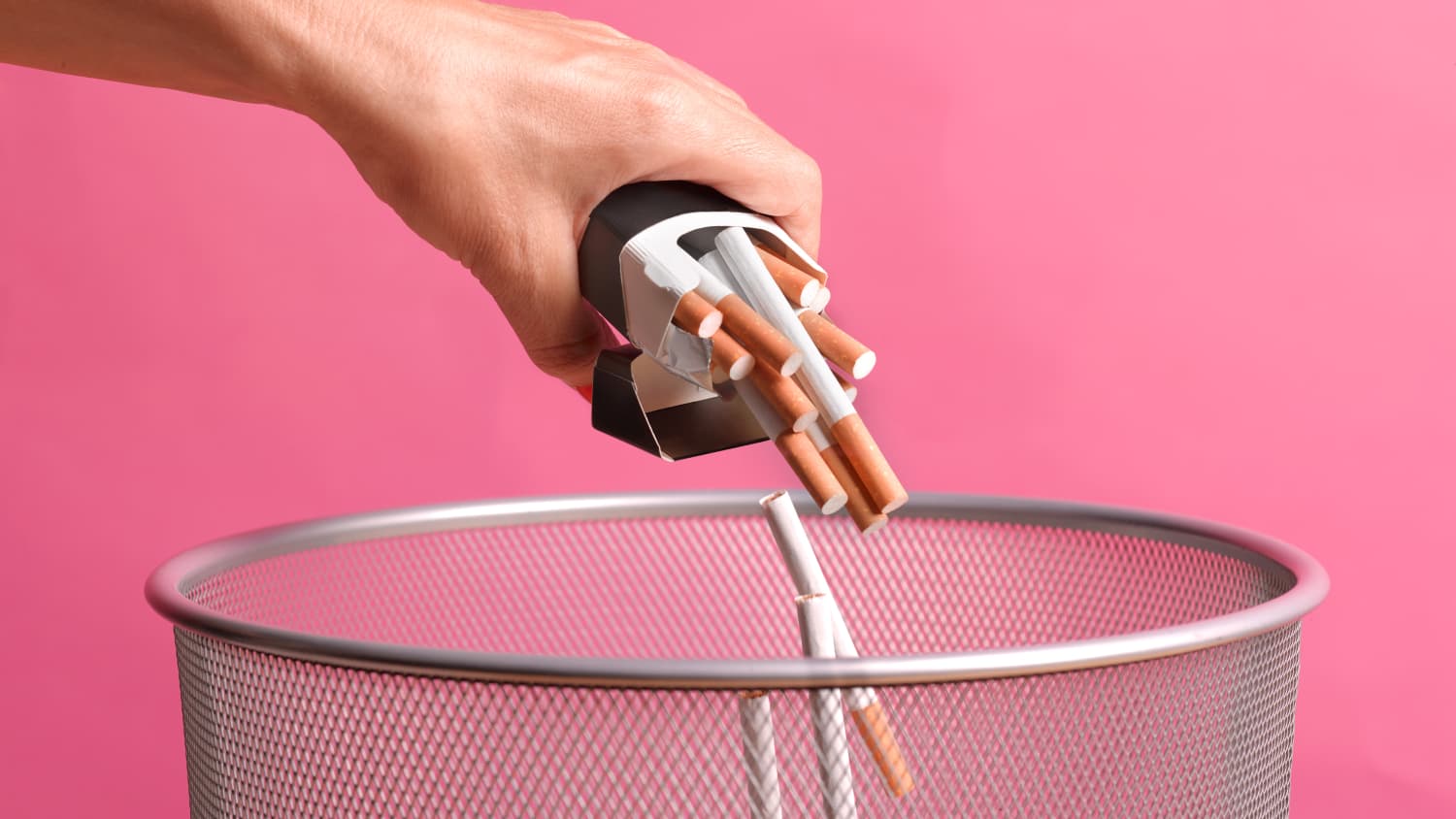 A woman quitting smoking tosses her cigarettes in the trash.