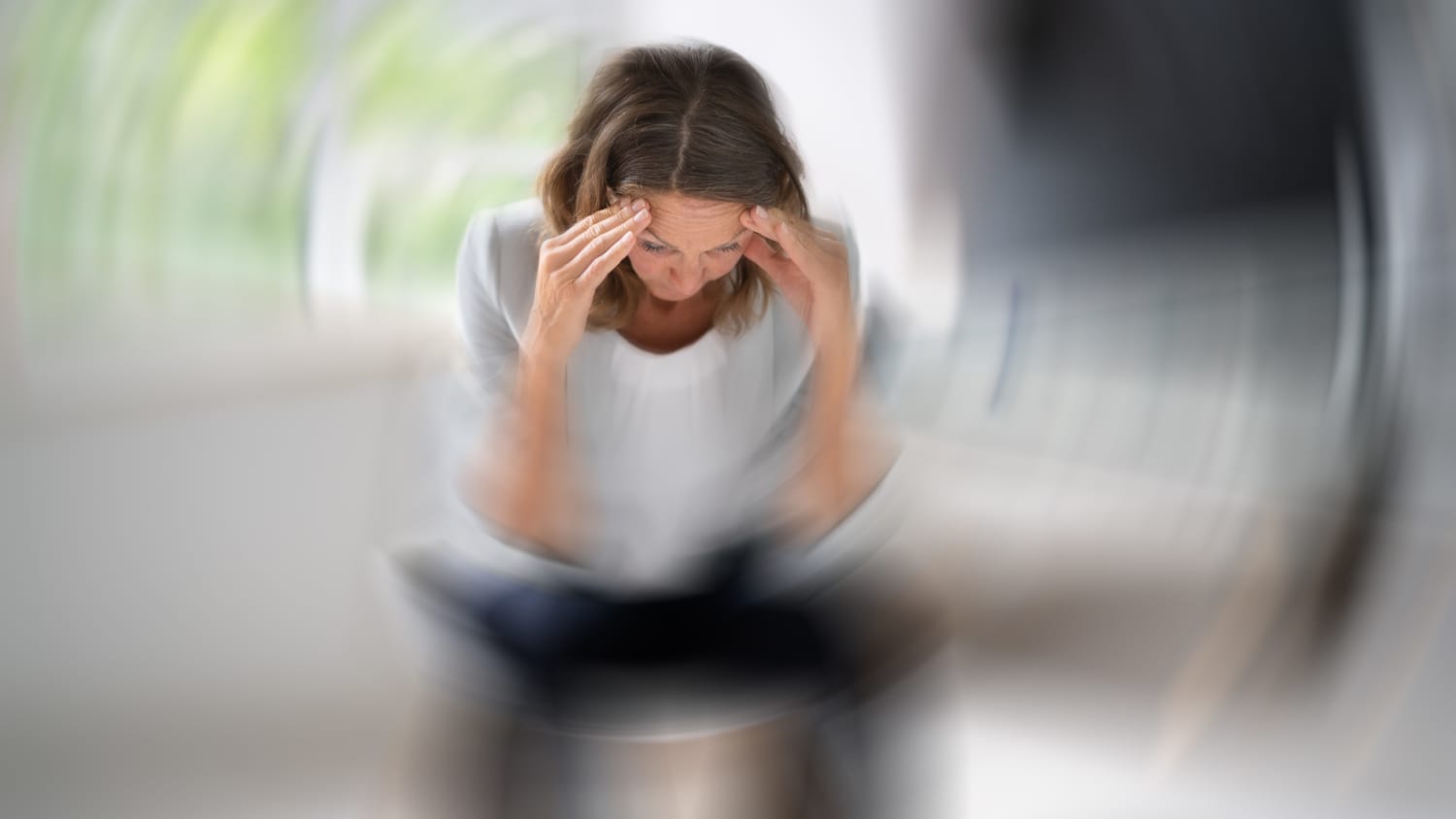 A woman holds her hands to her temples because she is feeling dizzy, possibly from a transient ischemic attack (TIA).
